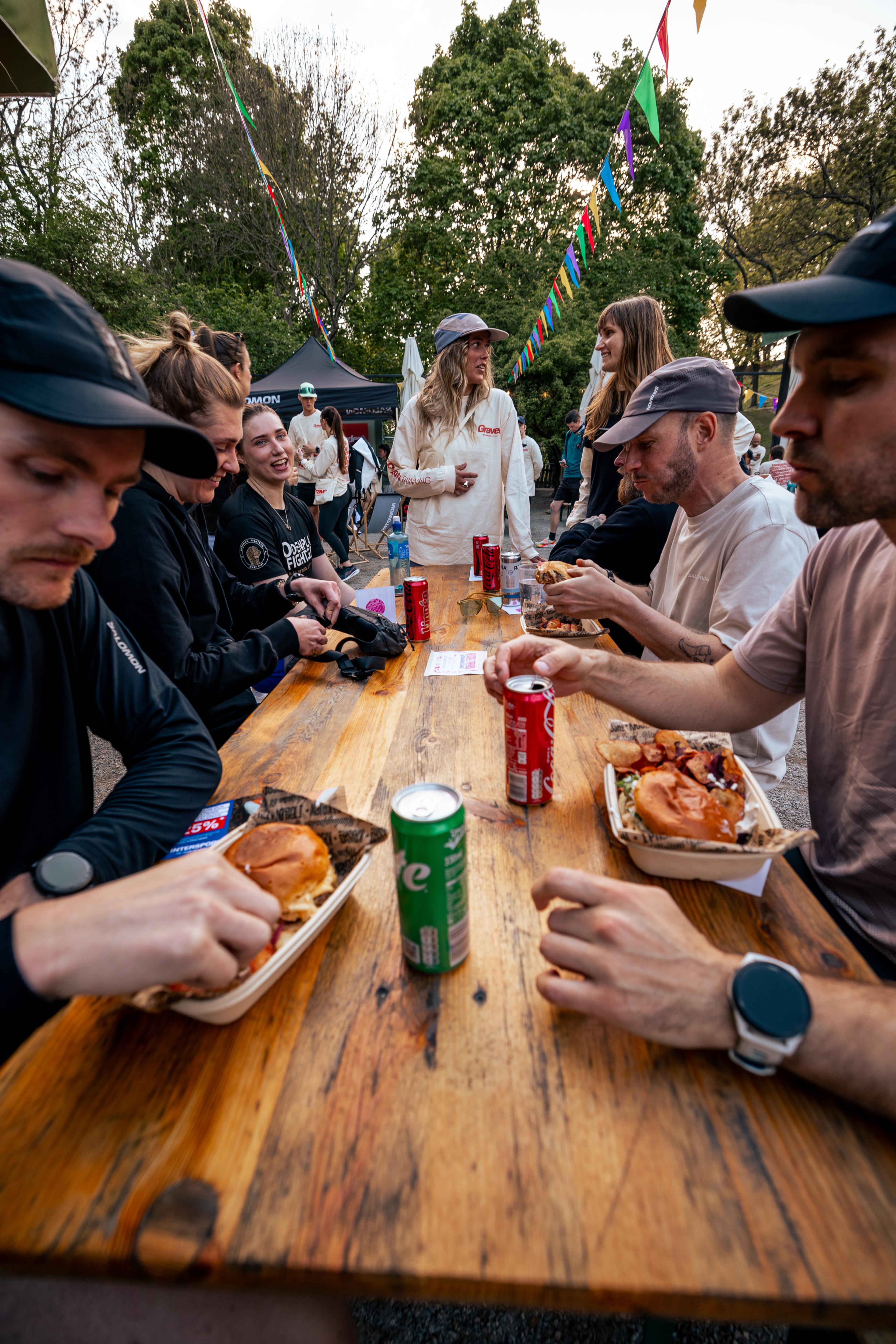 a group of people are sitting at a table eating food and drinking coke