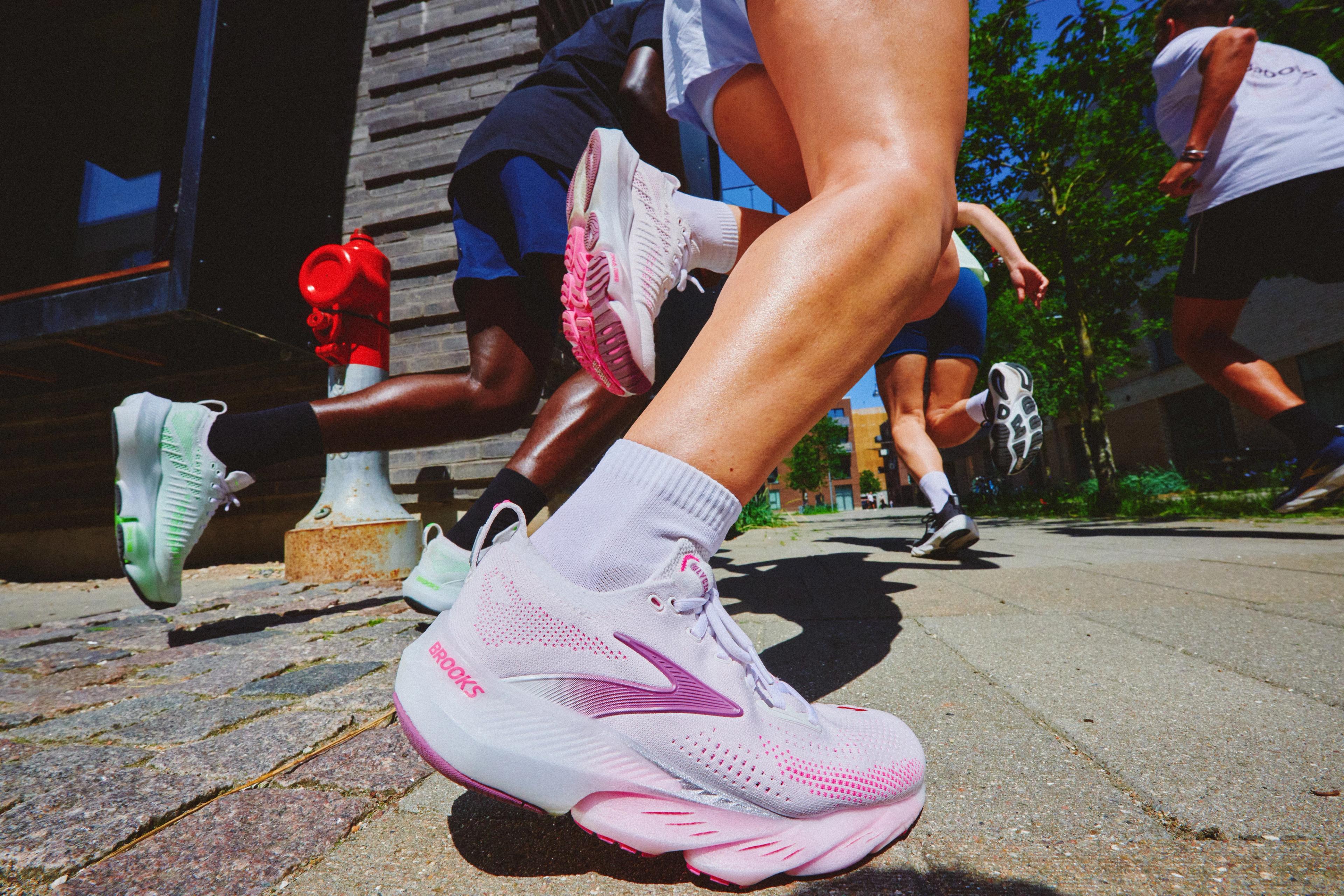 Low-angle shot of multiple runners in Brooks shoes mid-stride on a paved path.