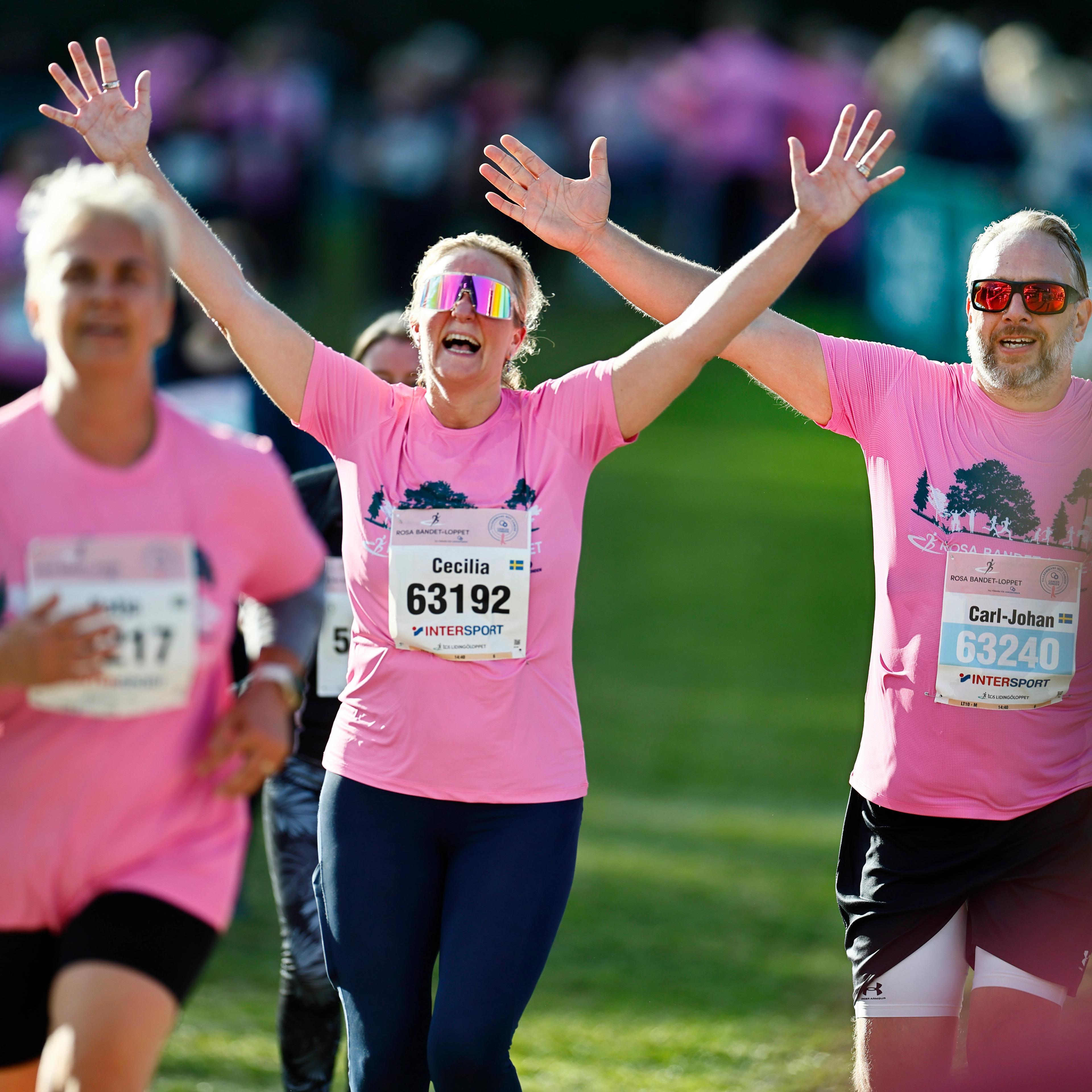 Runners in pink shirts celebrate with raised arms during a race.