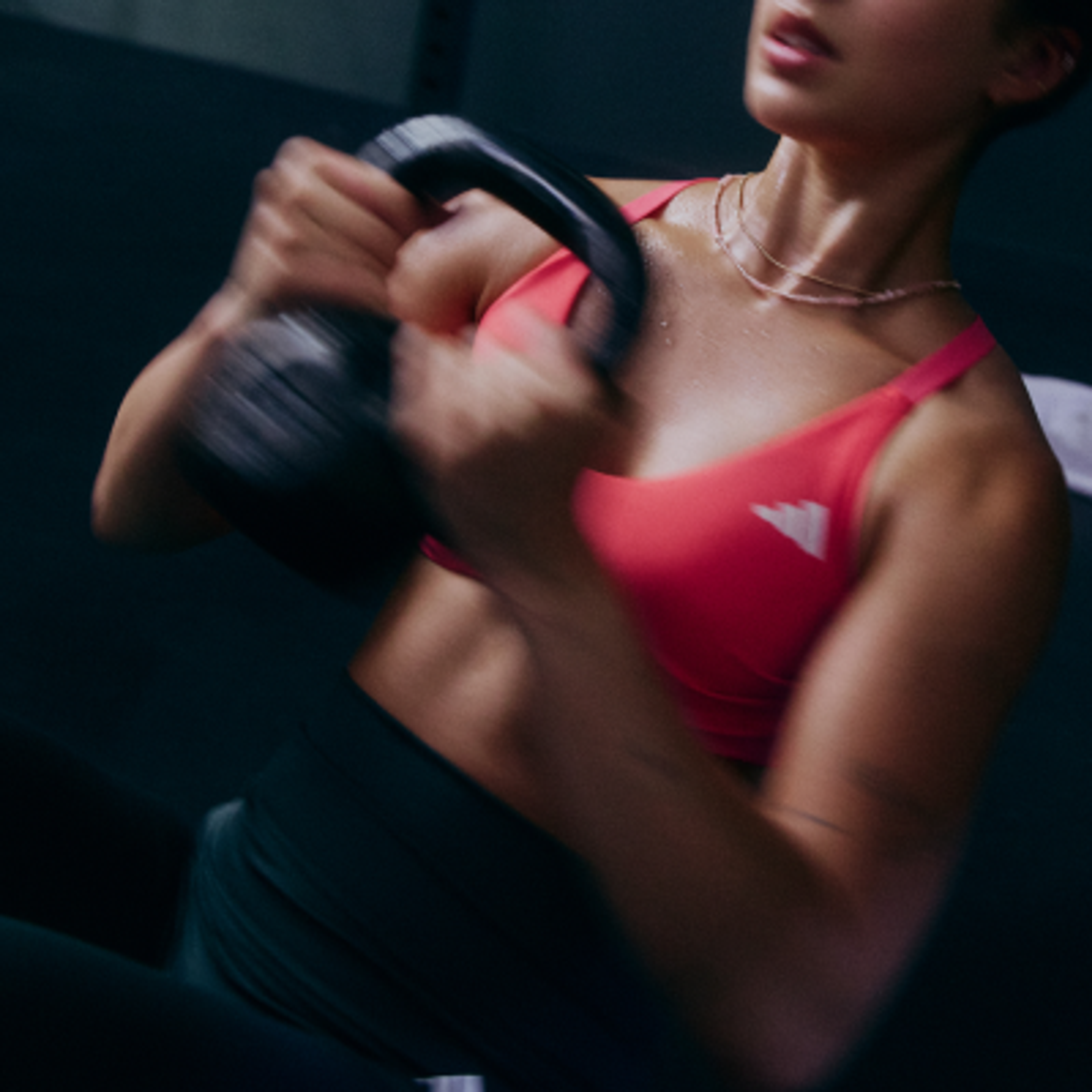 A sweaty person in a pink sports bra performing a kettlebell exercise, depicted with motion blur.