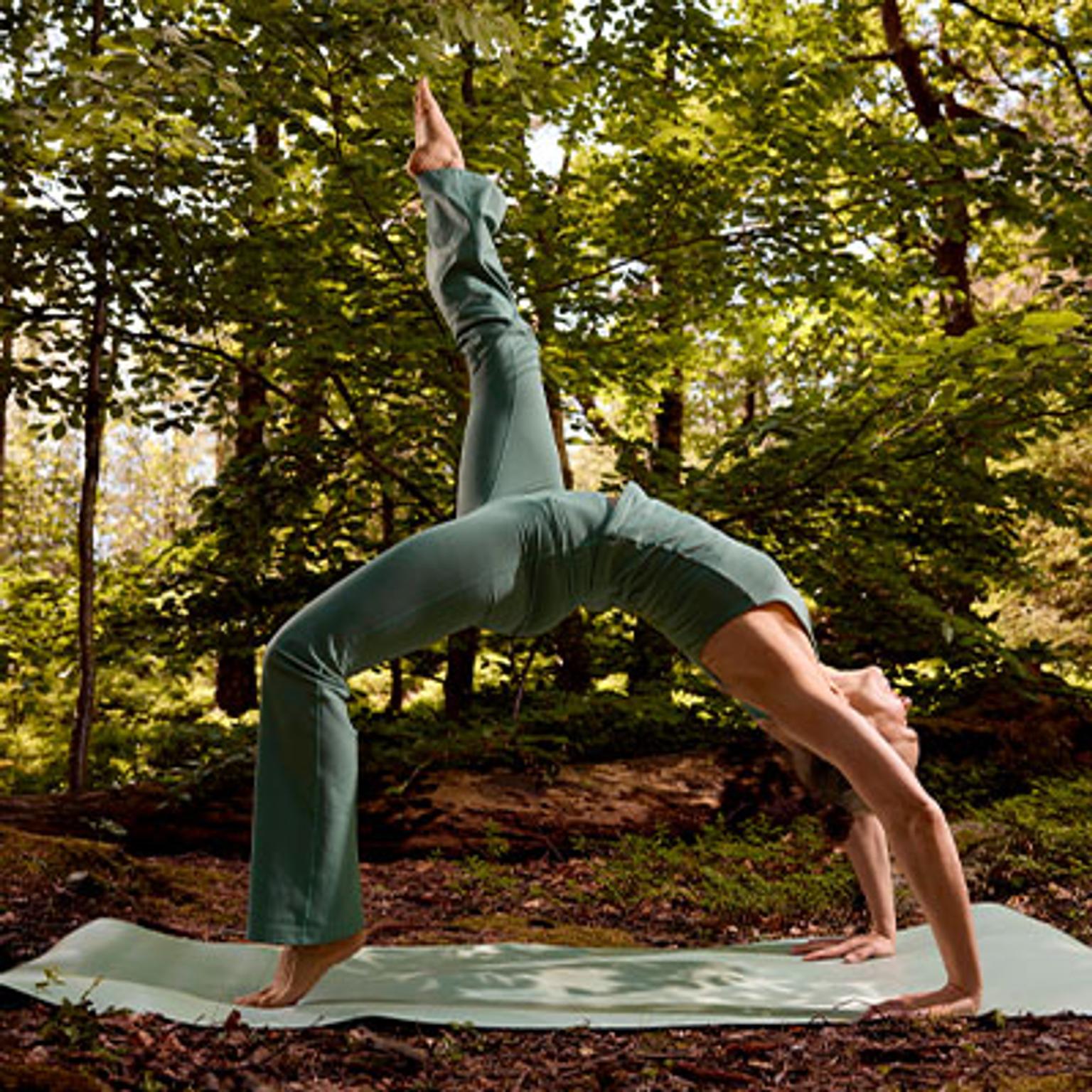 a woman is doing a yoga pose on a yoga mat in the woods .