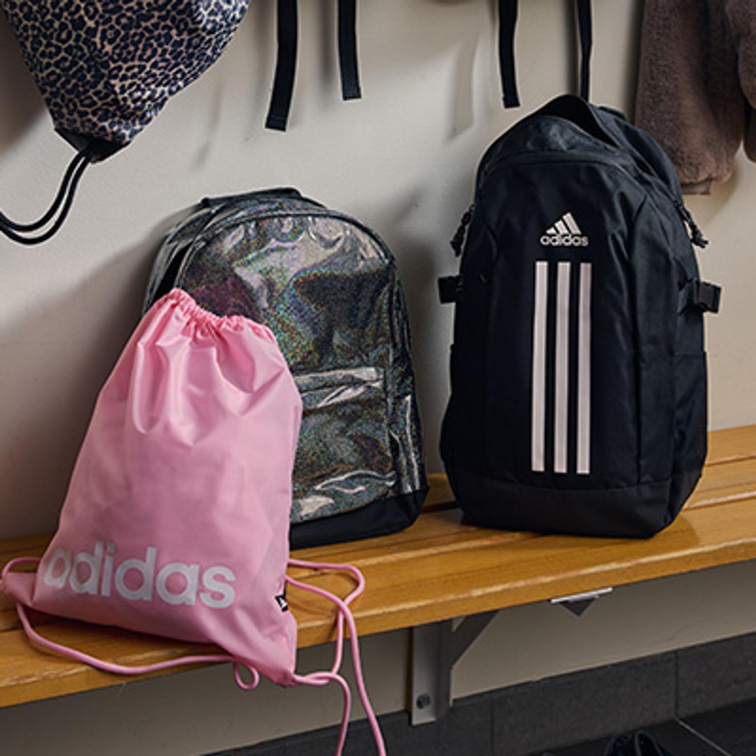 two backpacks and a pink drawstring bag are sitting on a wooden bench .