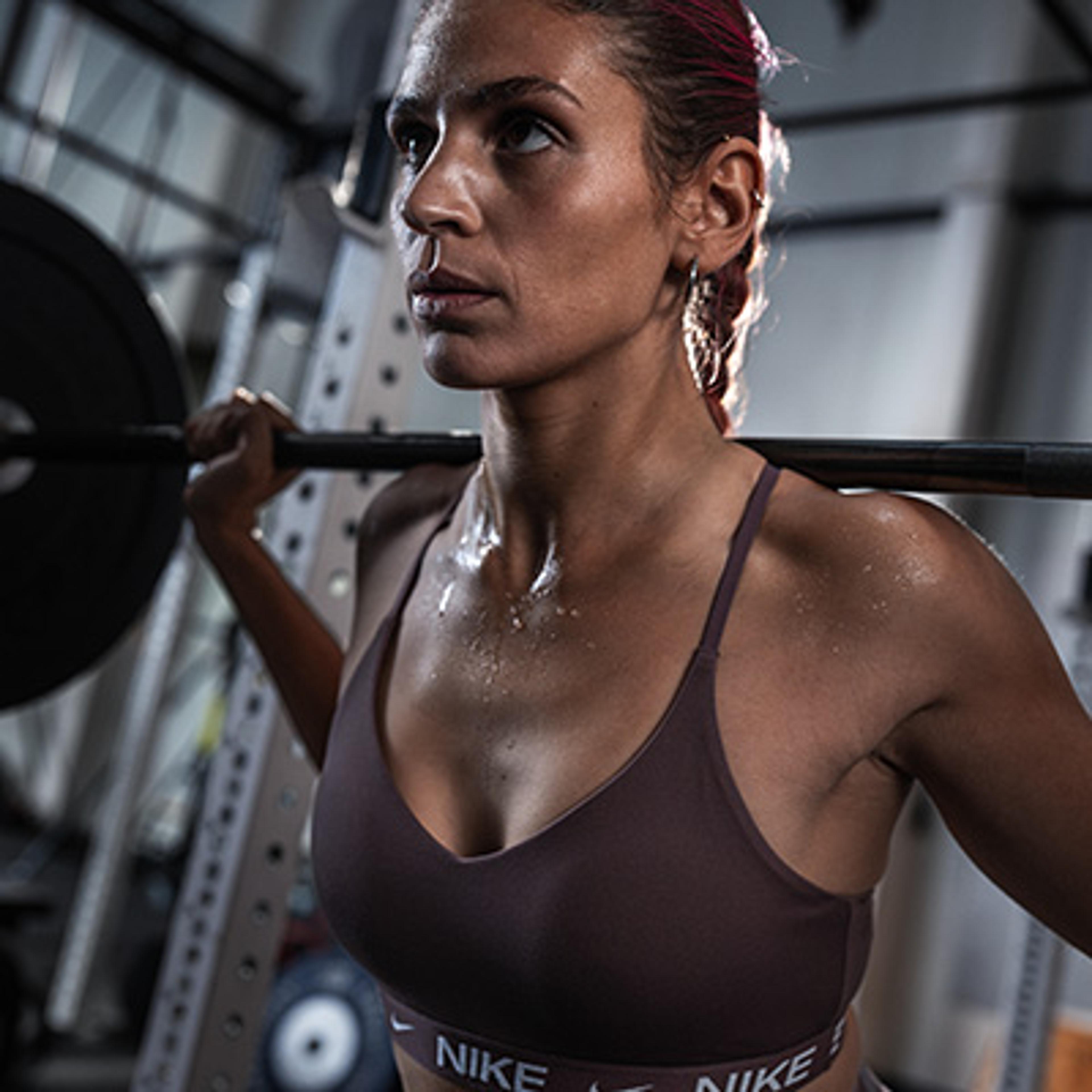 A determined, sweaty woman with a barbell on her shoulders.