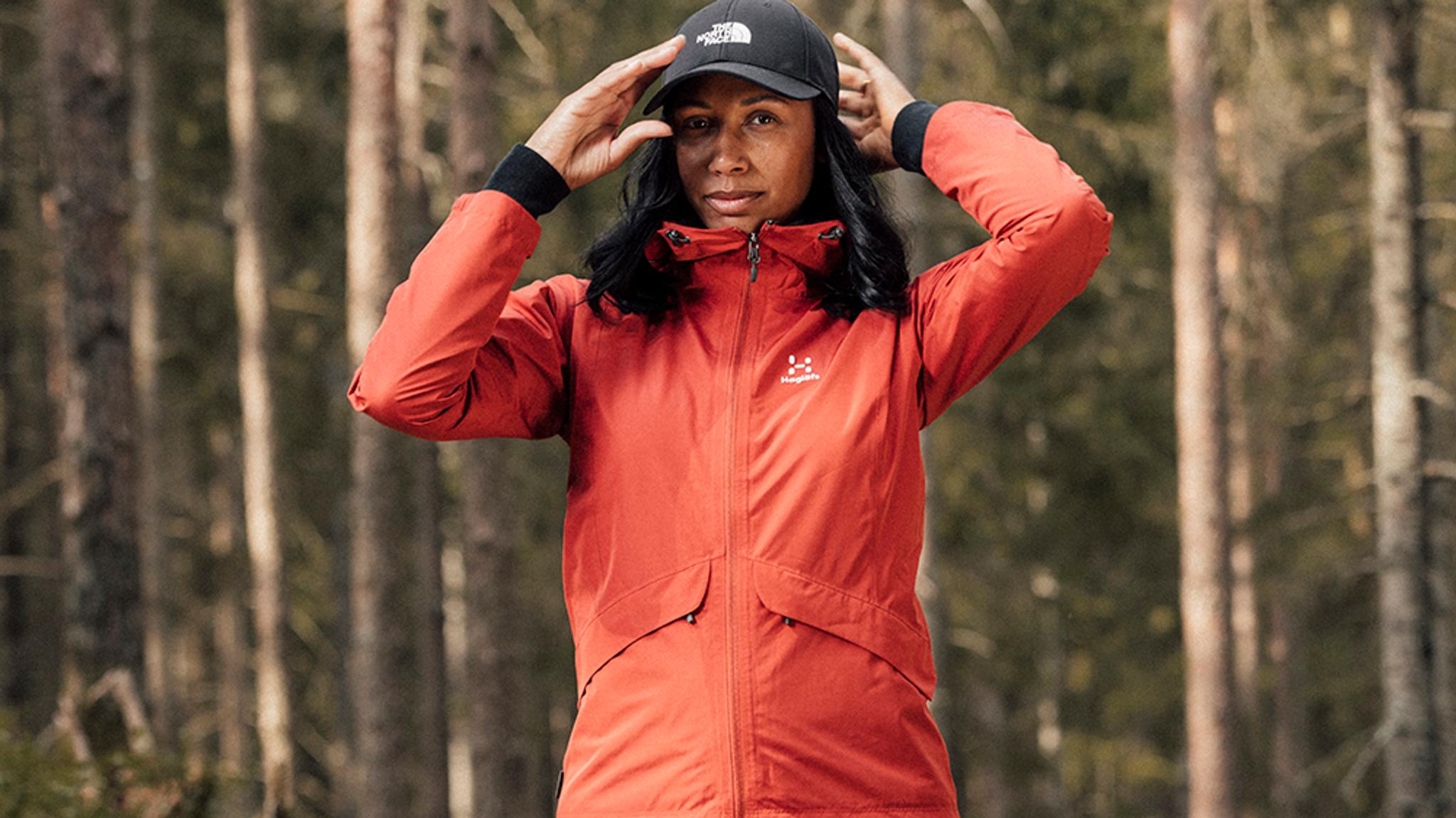 a woman wearing a red jacket and a black hat is standing in the woods .
