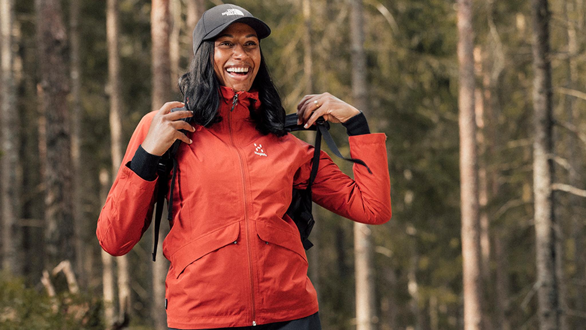 a woman wearing a red jacket and a black hat is standing in the woods .