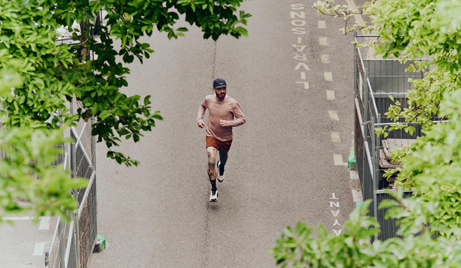 Bearded man running on a paved road, viewed from above, surrounded by green foliage.