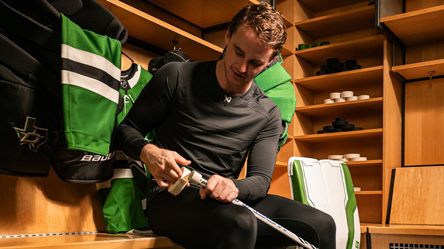 a hockey player is sitting on a bench in a locker room holding a hockey stick .