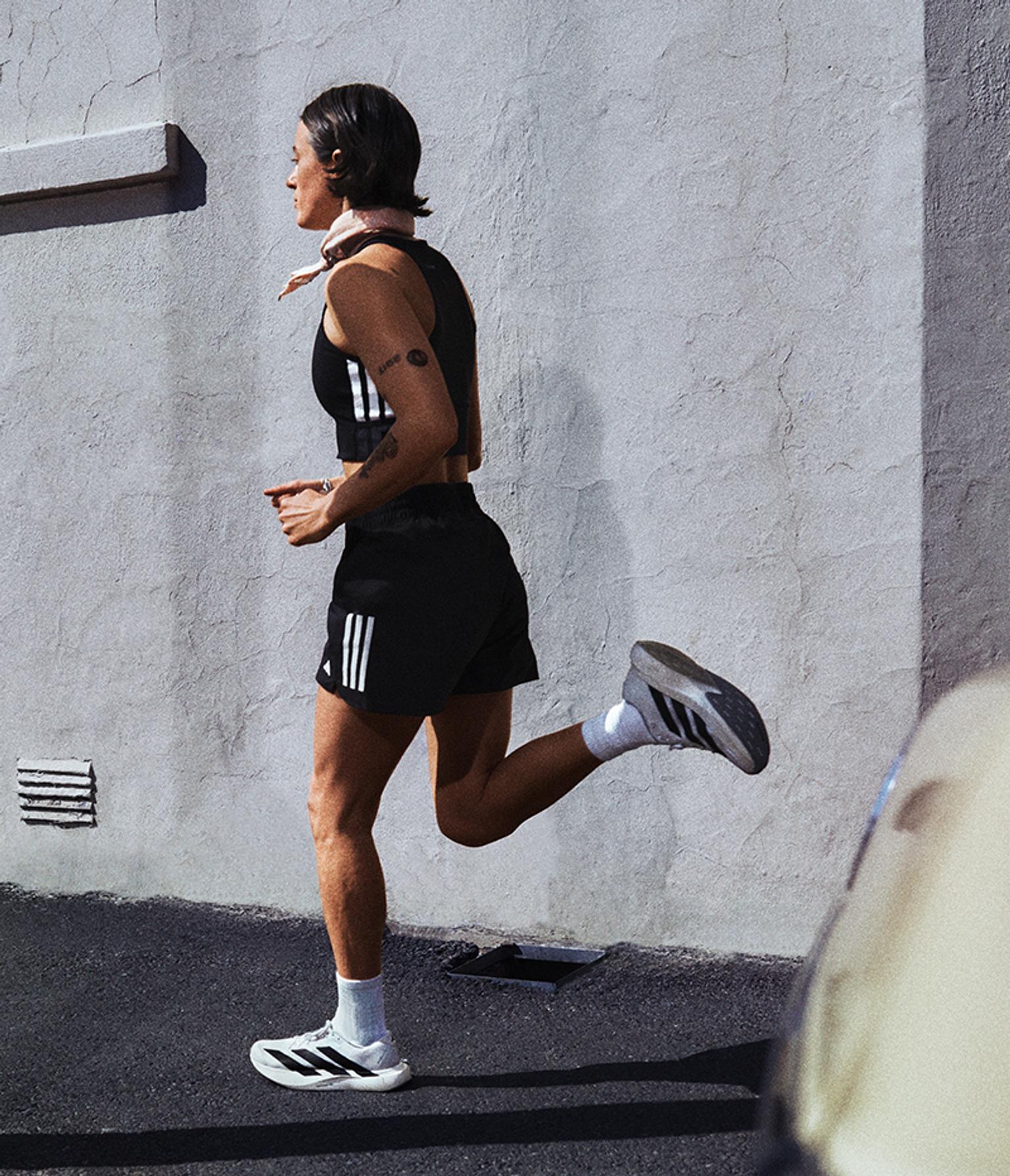 a woman is running on a sidewalk in front of a white wall .