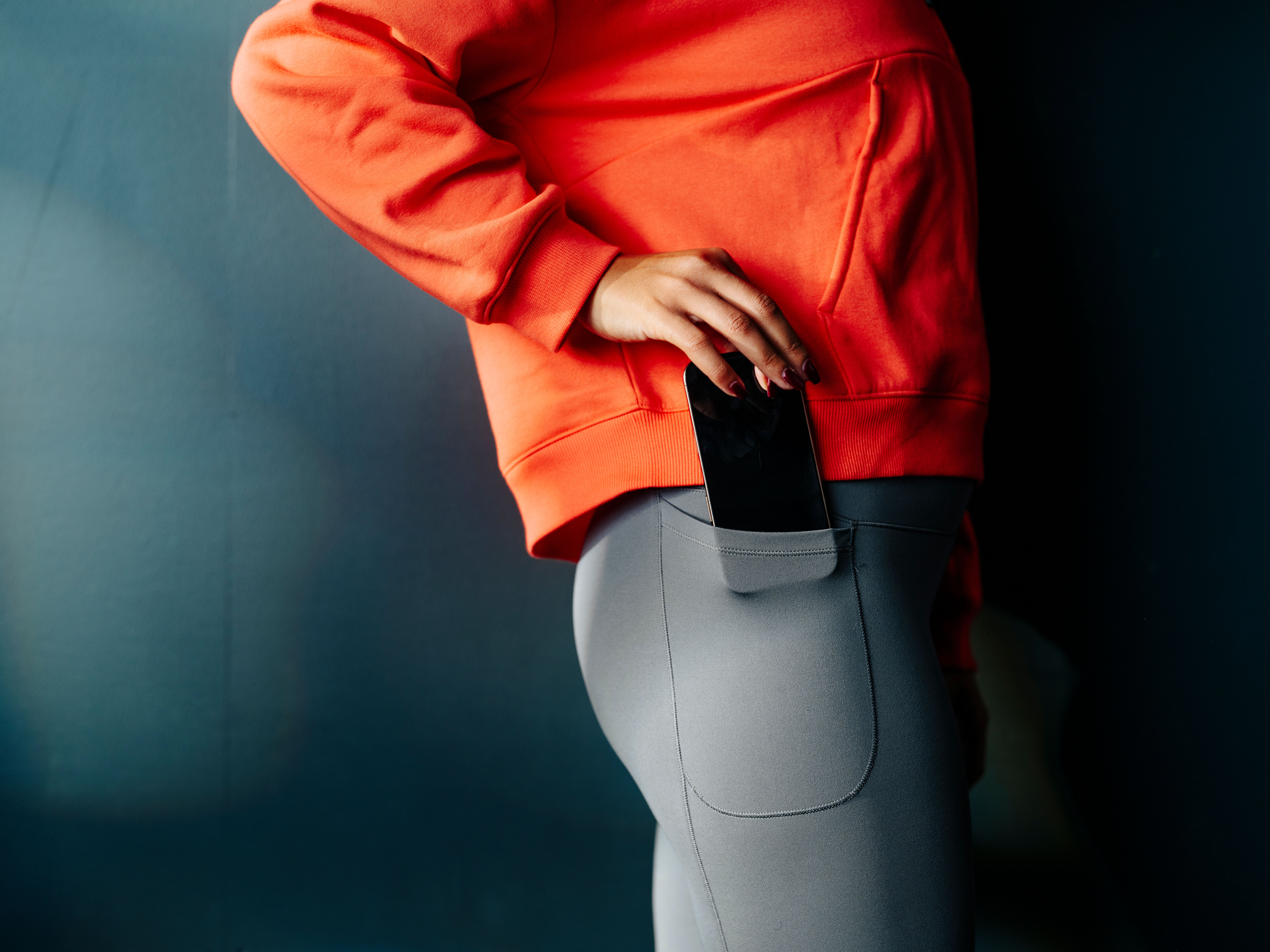 A hand places a smartphone into the side pocket of gray leggings.