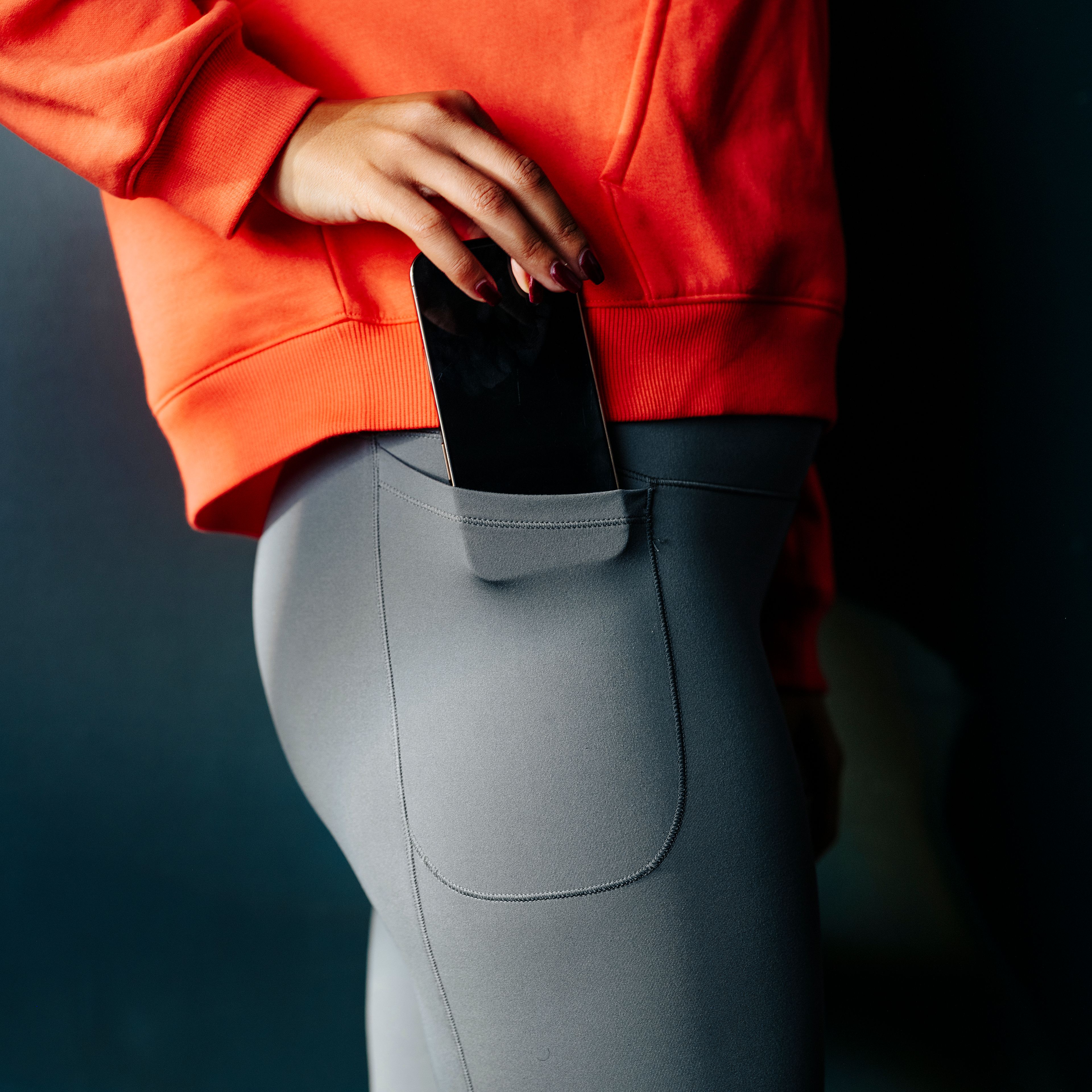 A hand places a smartphone into the side pocket of gray leggings.