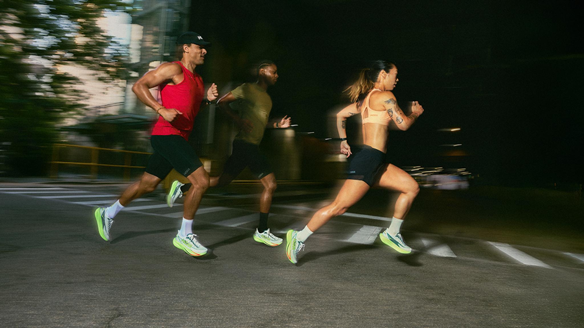 Three runners with motion blur wearing bright shoes on a city street at night.