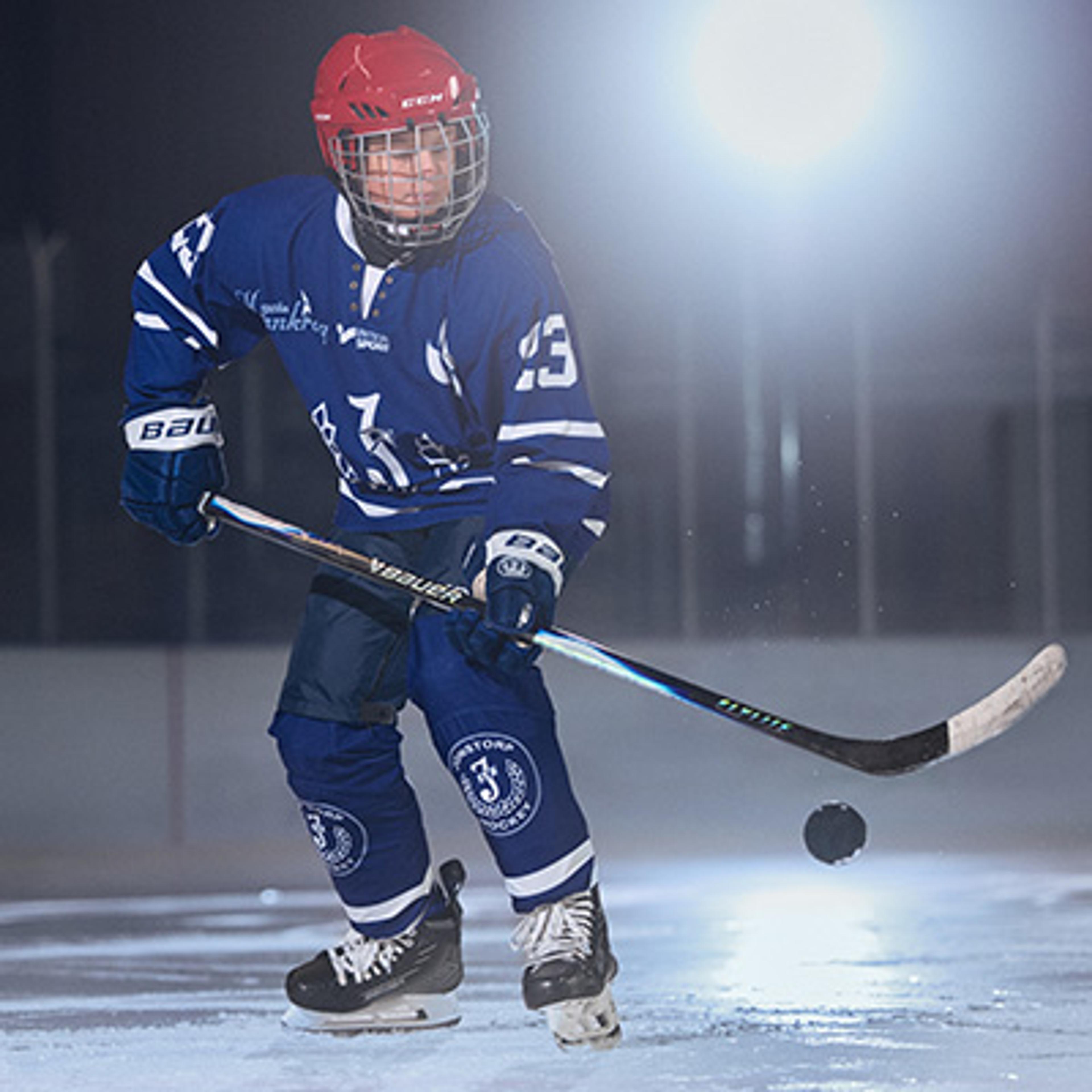 A hockey player in a blue jersey and red helmet stickhandles a puck on ice.