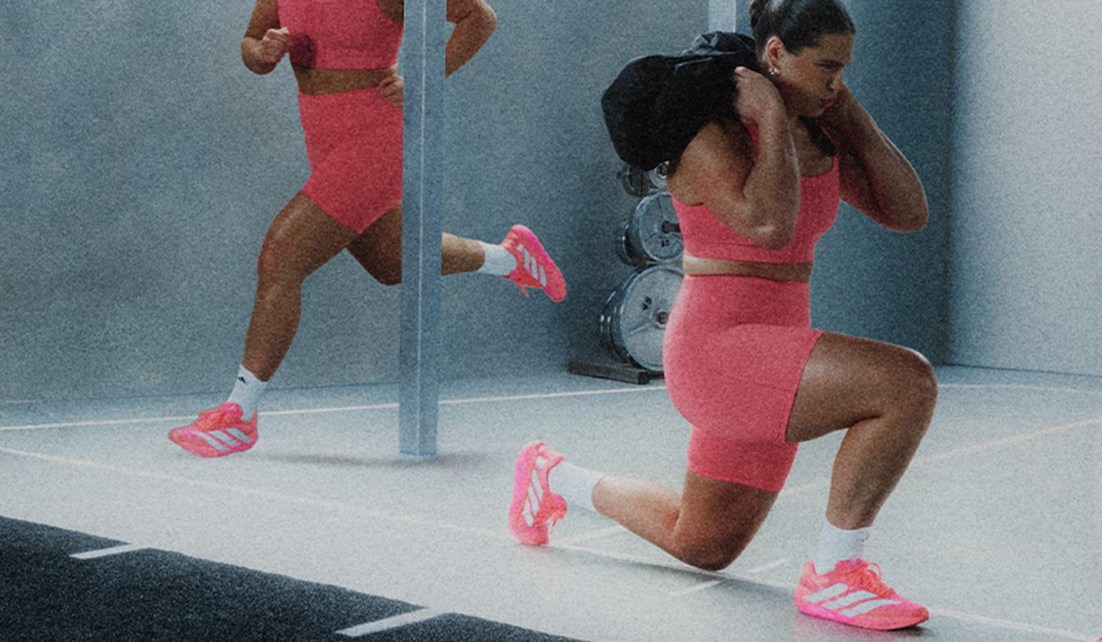 Woman in pink sports outfit lunging with a sandbag and running in a gym.