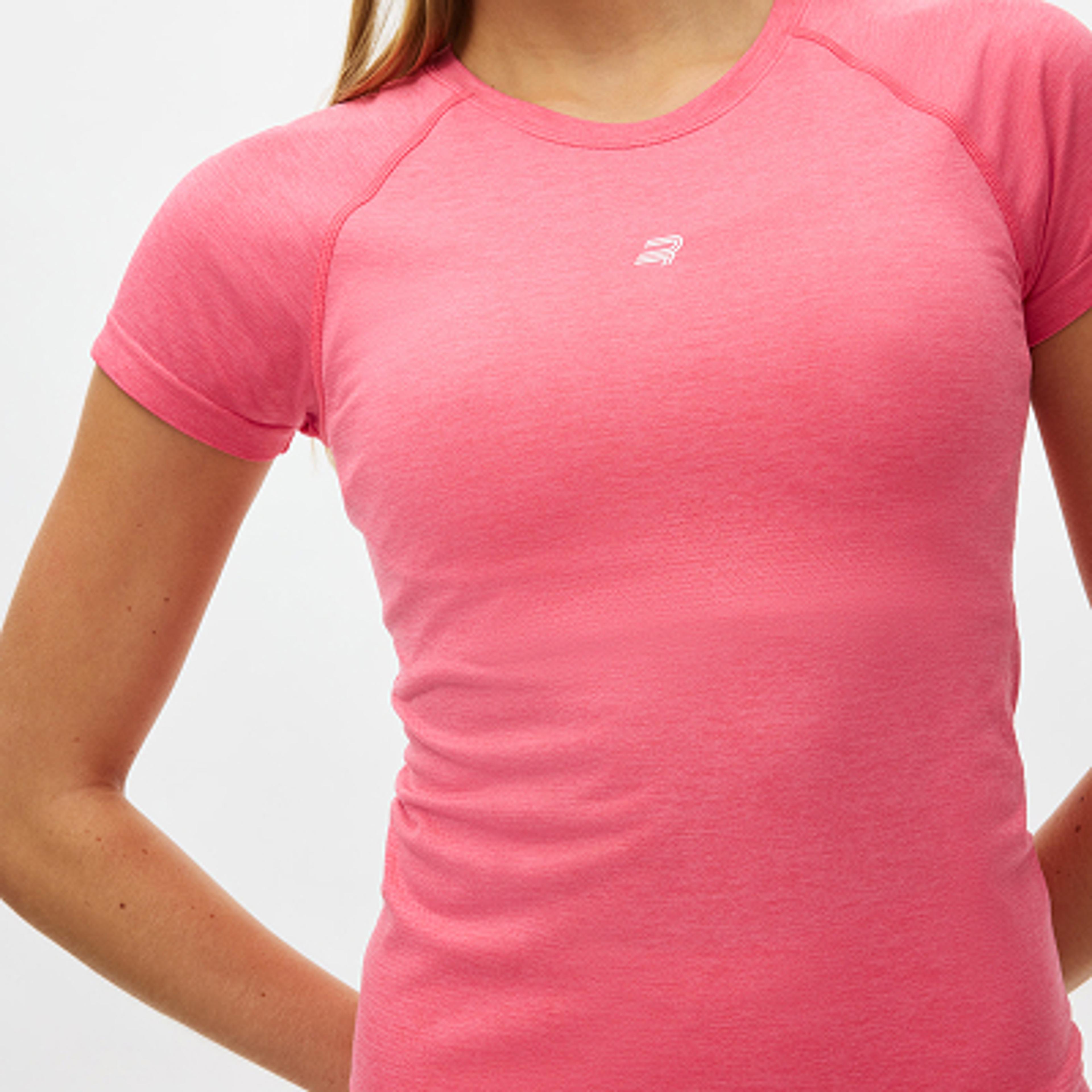 A woman wears a pink short-sleeved t-shirt with a white logo on the chest.
