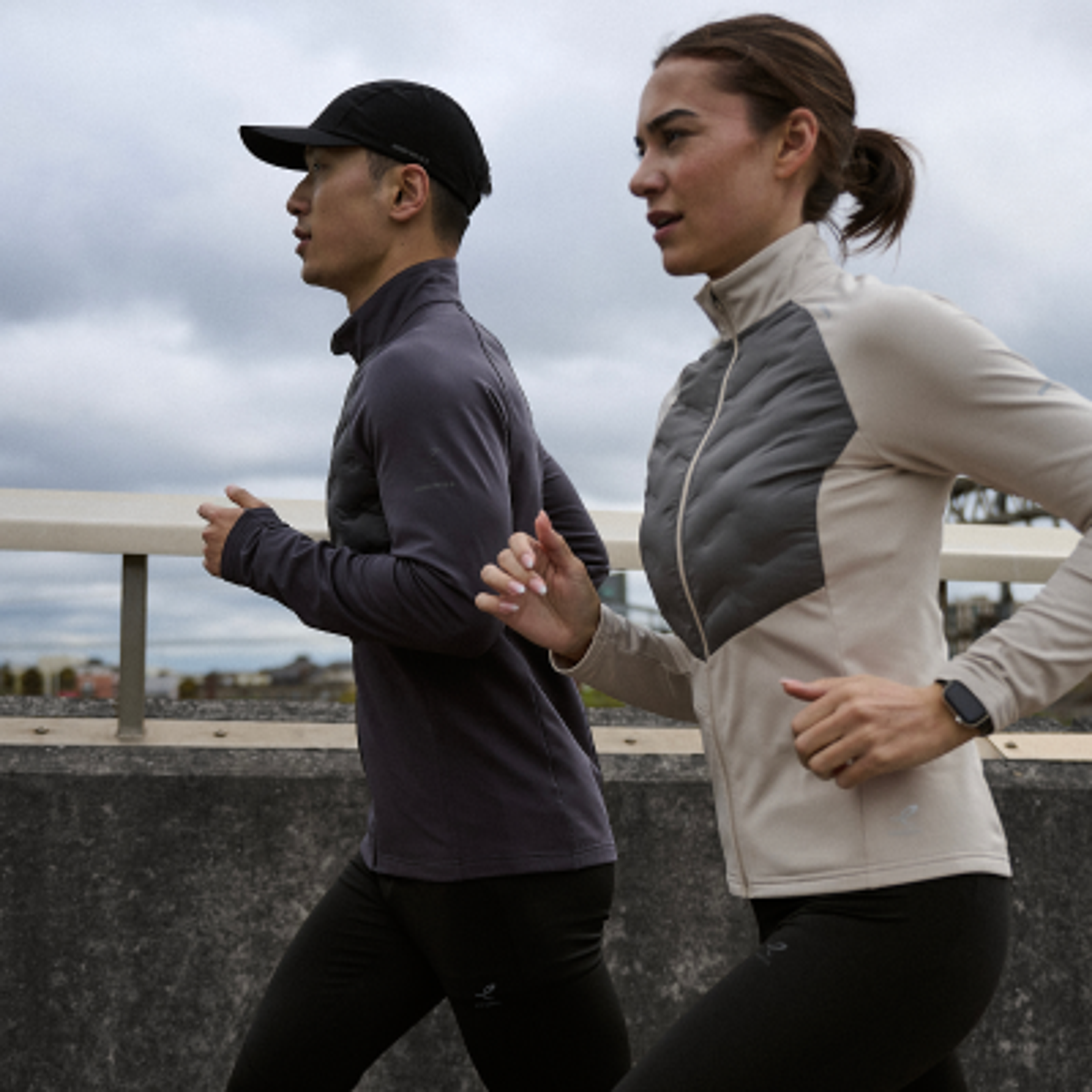 A man and a woman running outdoors in athletic jackets.