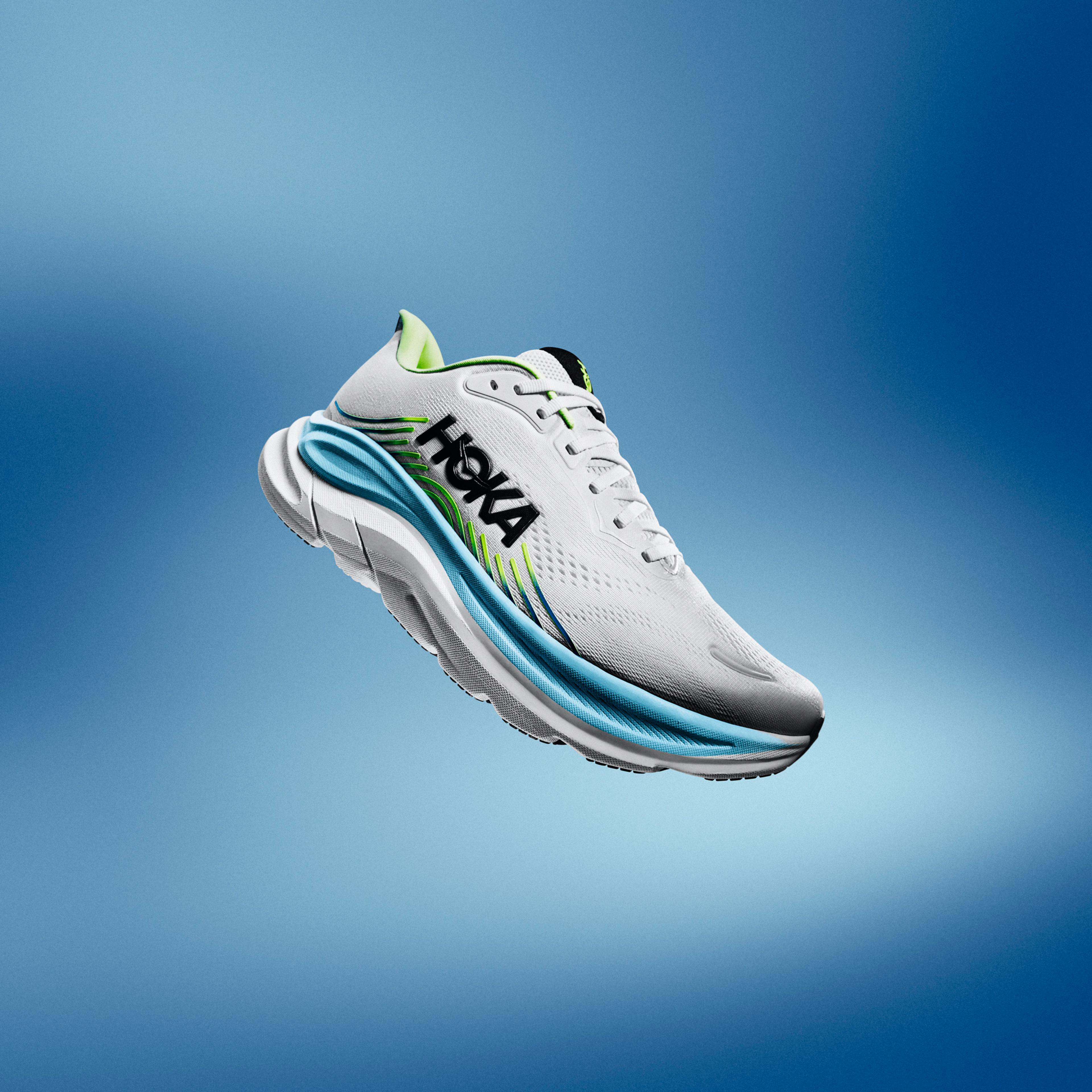 White Hoka running shoe with blue and green accents, floating on a blue gradient background.