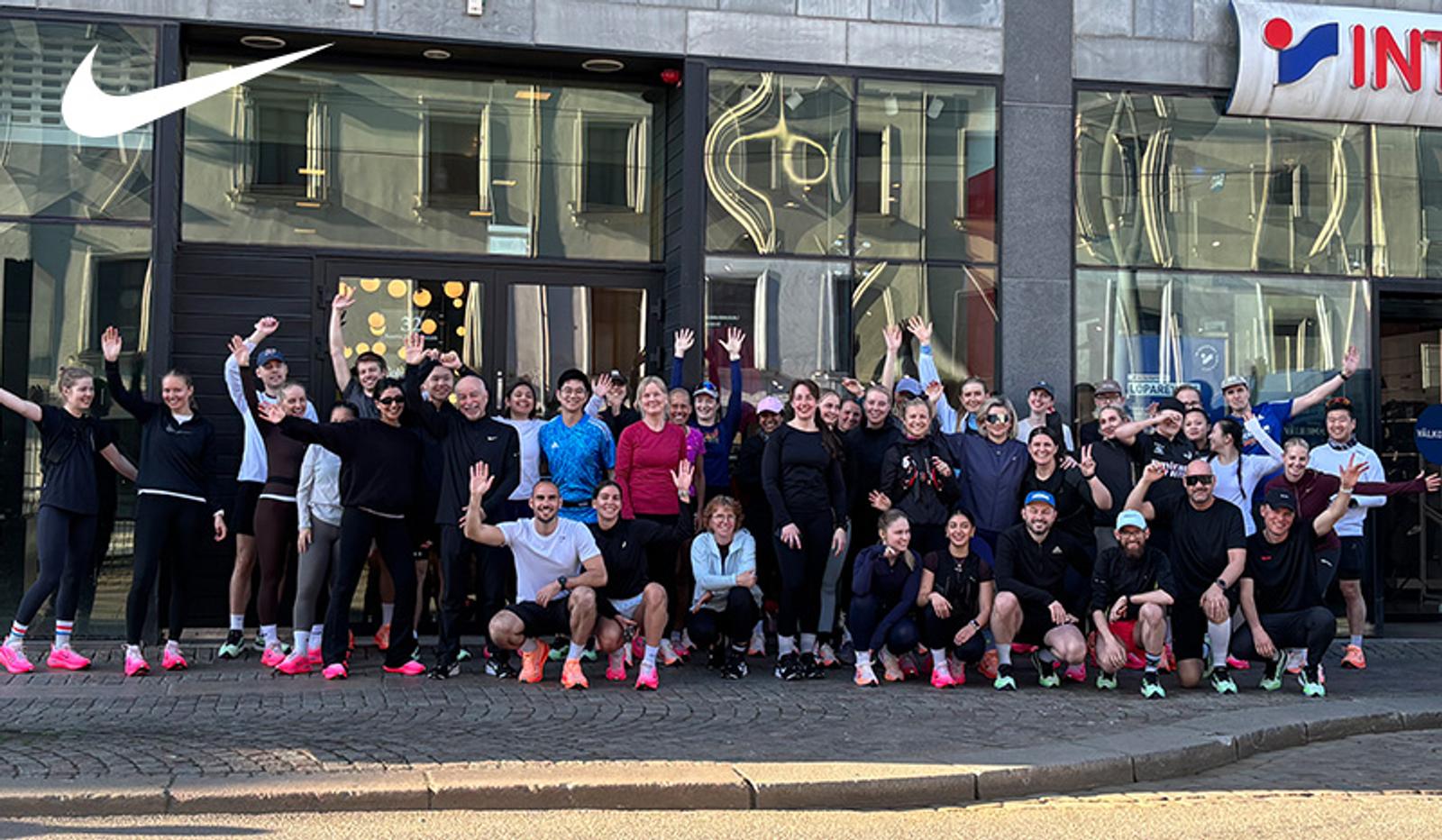 A group of people in athletic wear wave in front of Nike and Intersport stores.