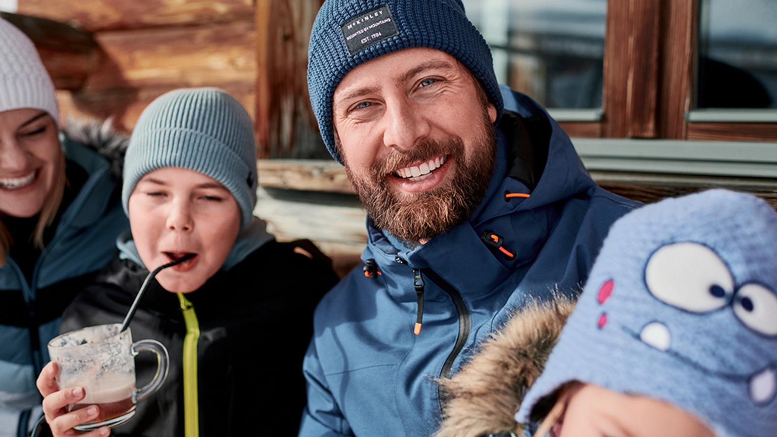 a man with a beard, hat and jackett is with his family in the winter .