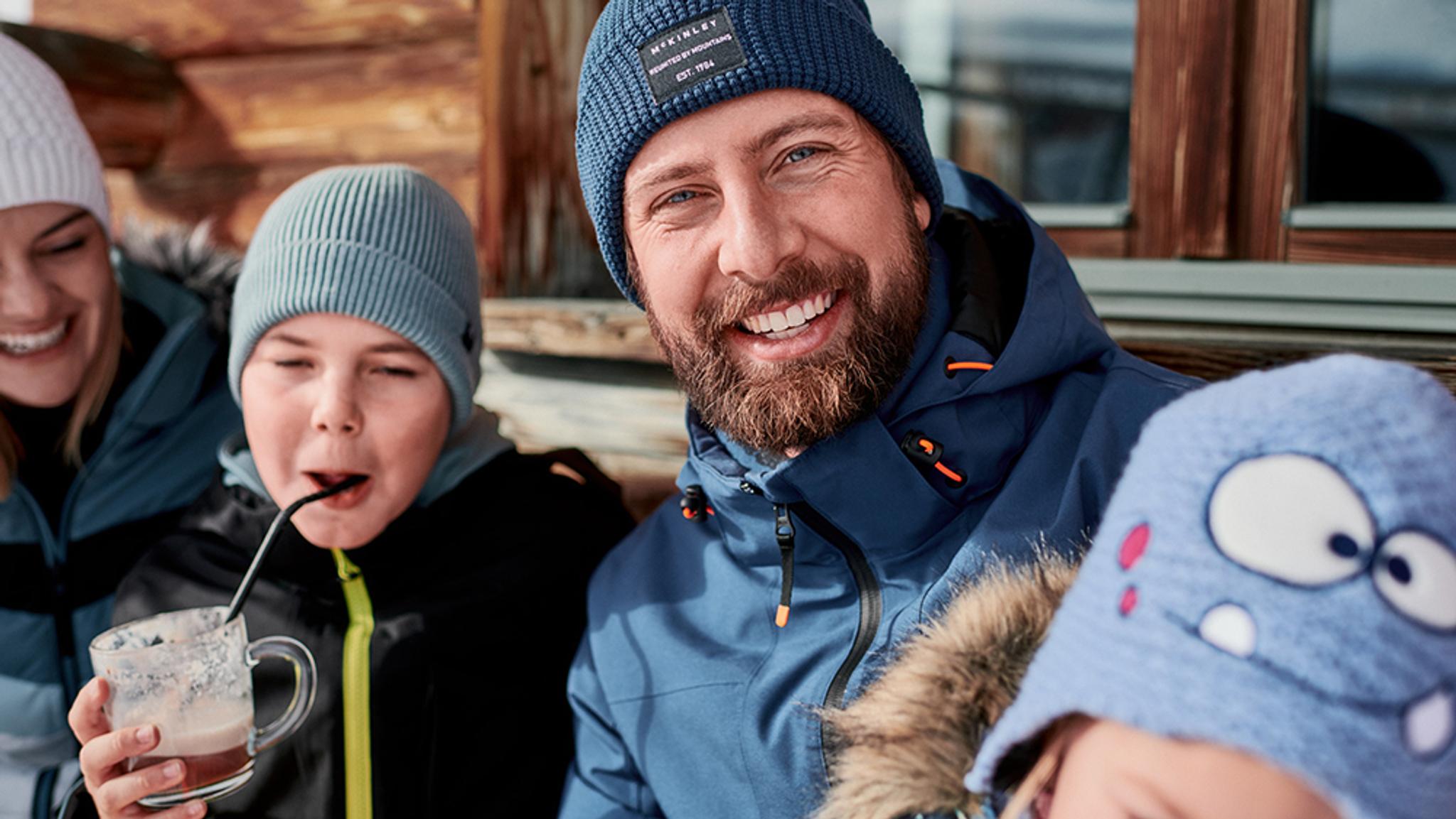 a man with a beard, hat and jackett is with his family in the winter .
