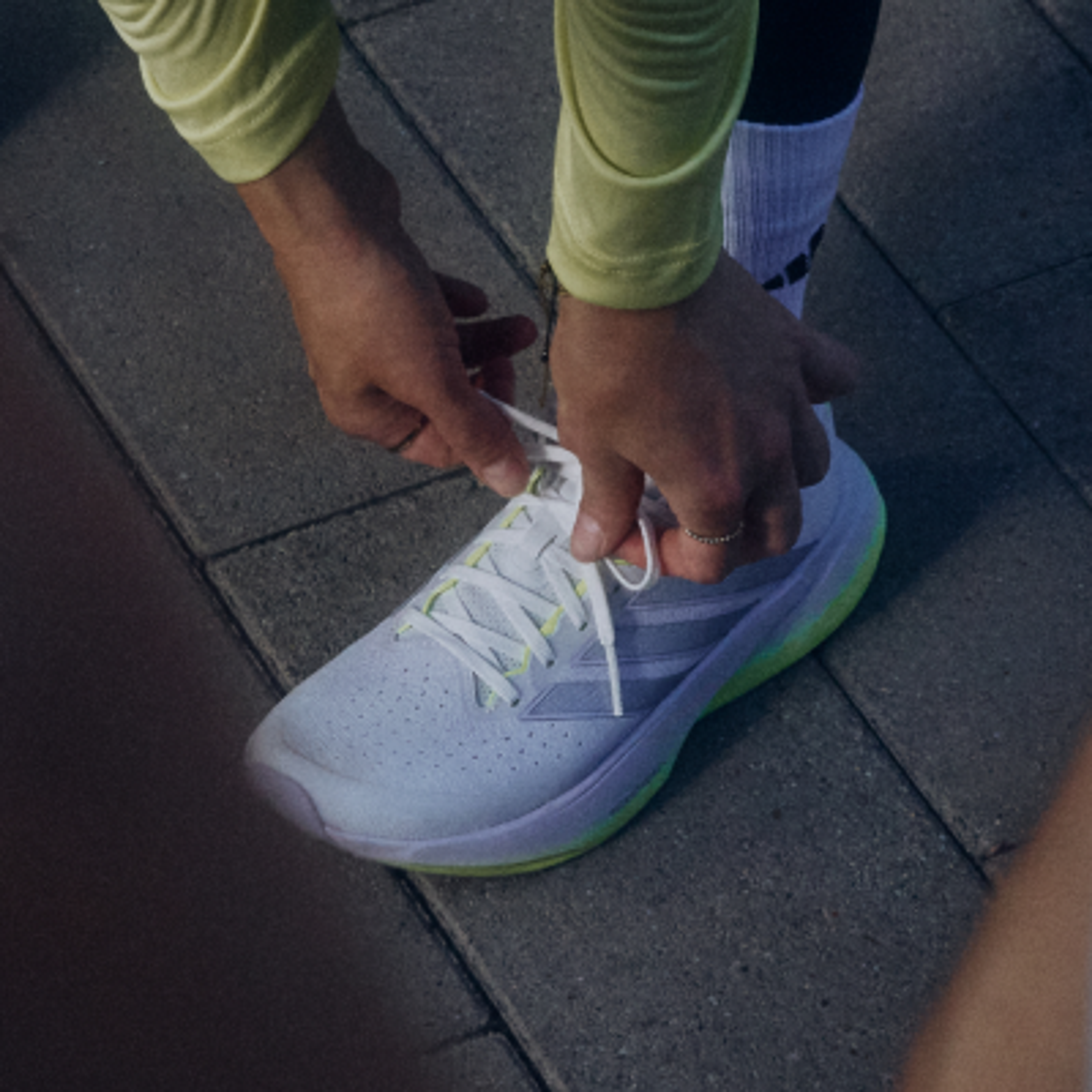 Close-up of hands tying the laces of a white and neon green running shoe.