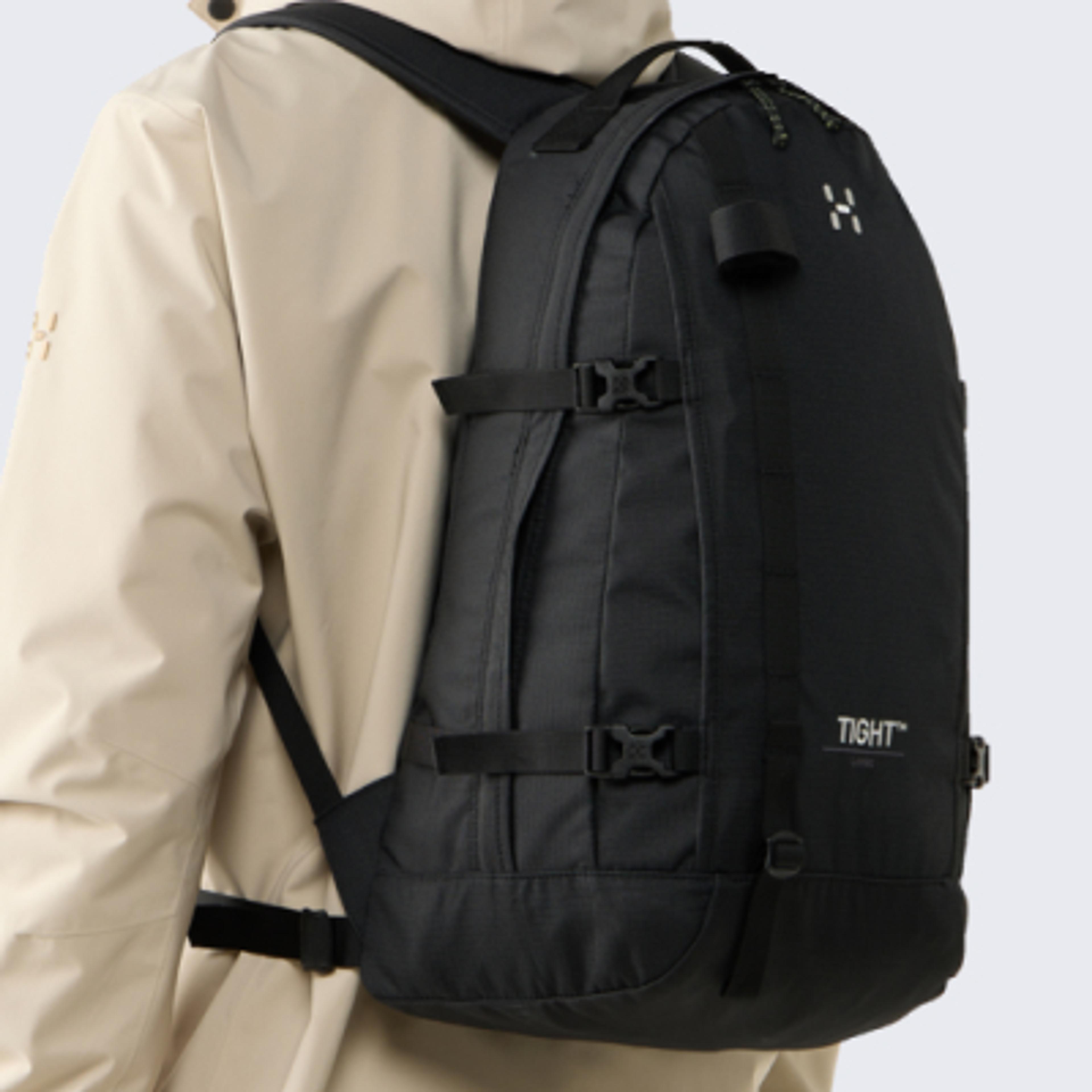 A person seen from the back wearing a light jacket and a black Haglöfs Tight backpack.