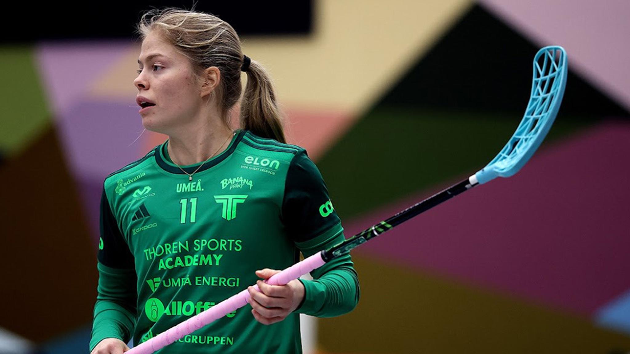 a woman in a green shirt is holding a lacrosse stick .
