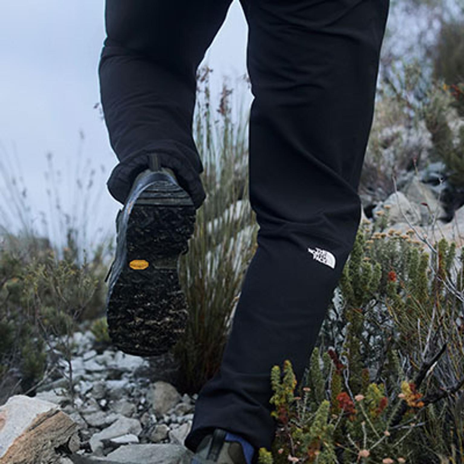 a person wearing the north face pants is walking on a rocky hillside .