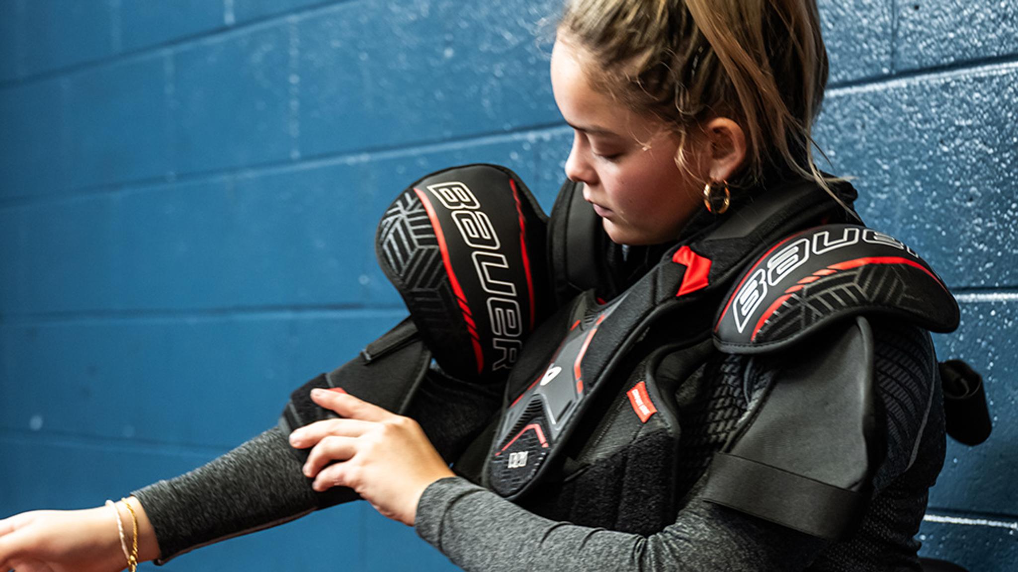 a young girl is wearing a hockey protective vest and elbow pads .