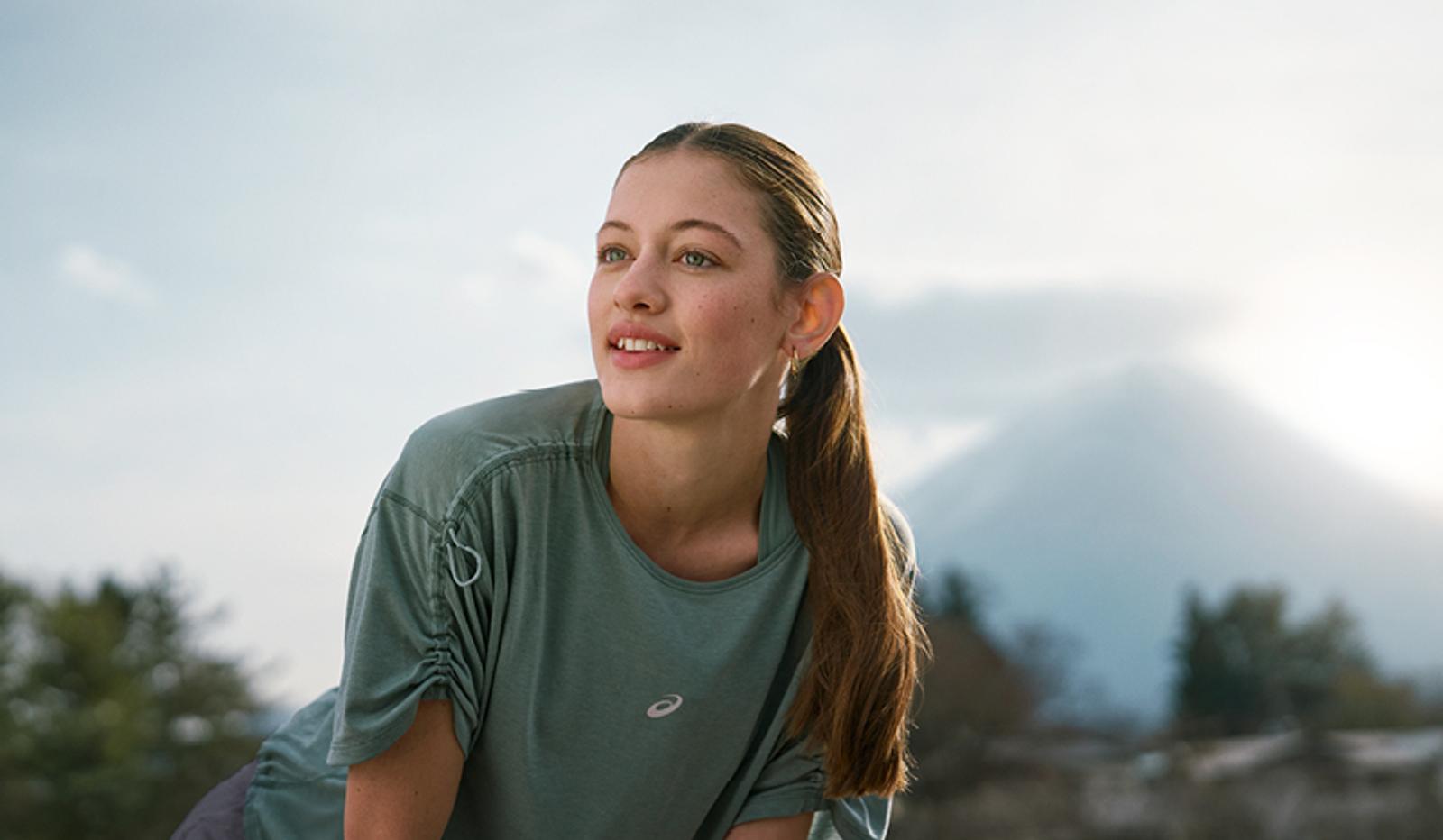 a young woman is stretching her legs in front of a mountain .