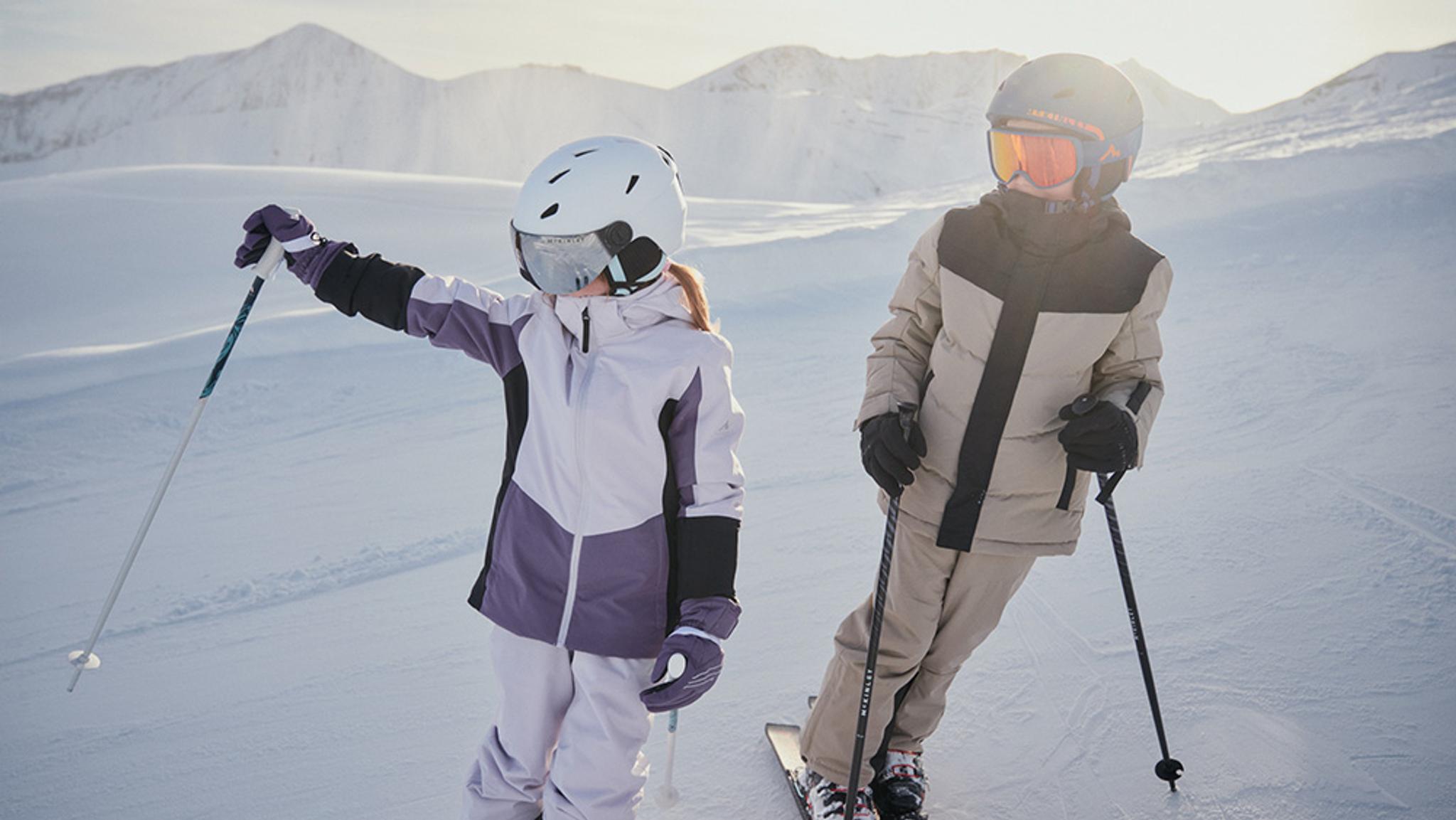 Two children in ski gear on a sunny, snow-covered mountain.