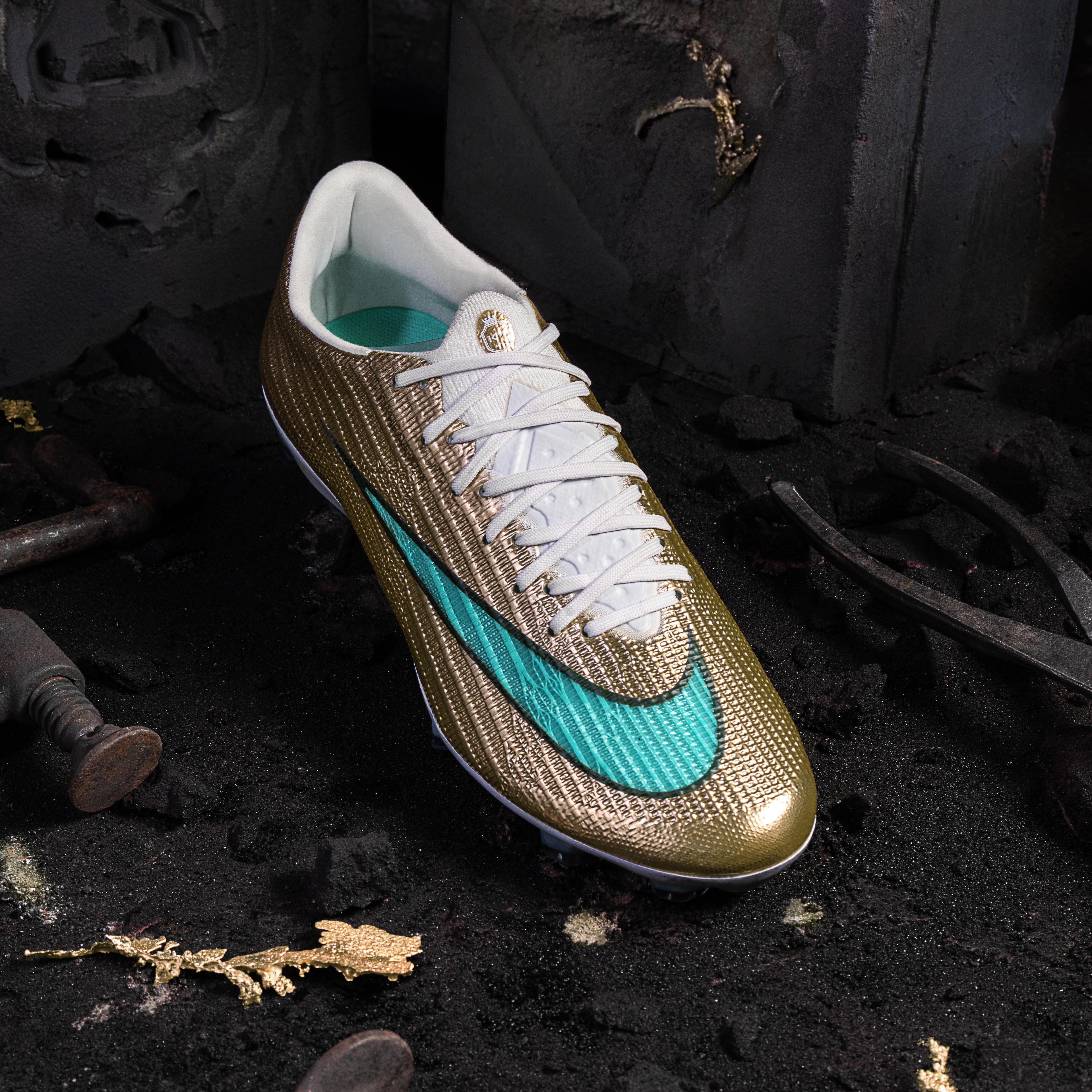 A gold soccer cleat with a teal Nike swoosh rests on a dark, textured surface scattered with gold fragments, in a dark industrial setting.