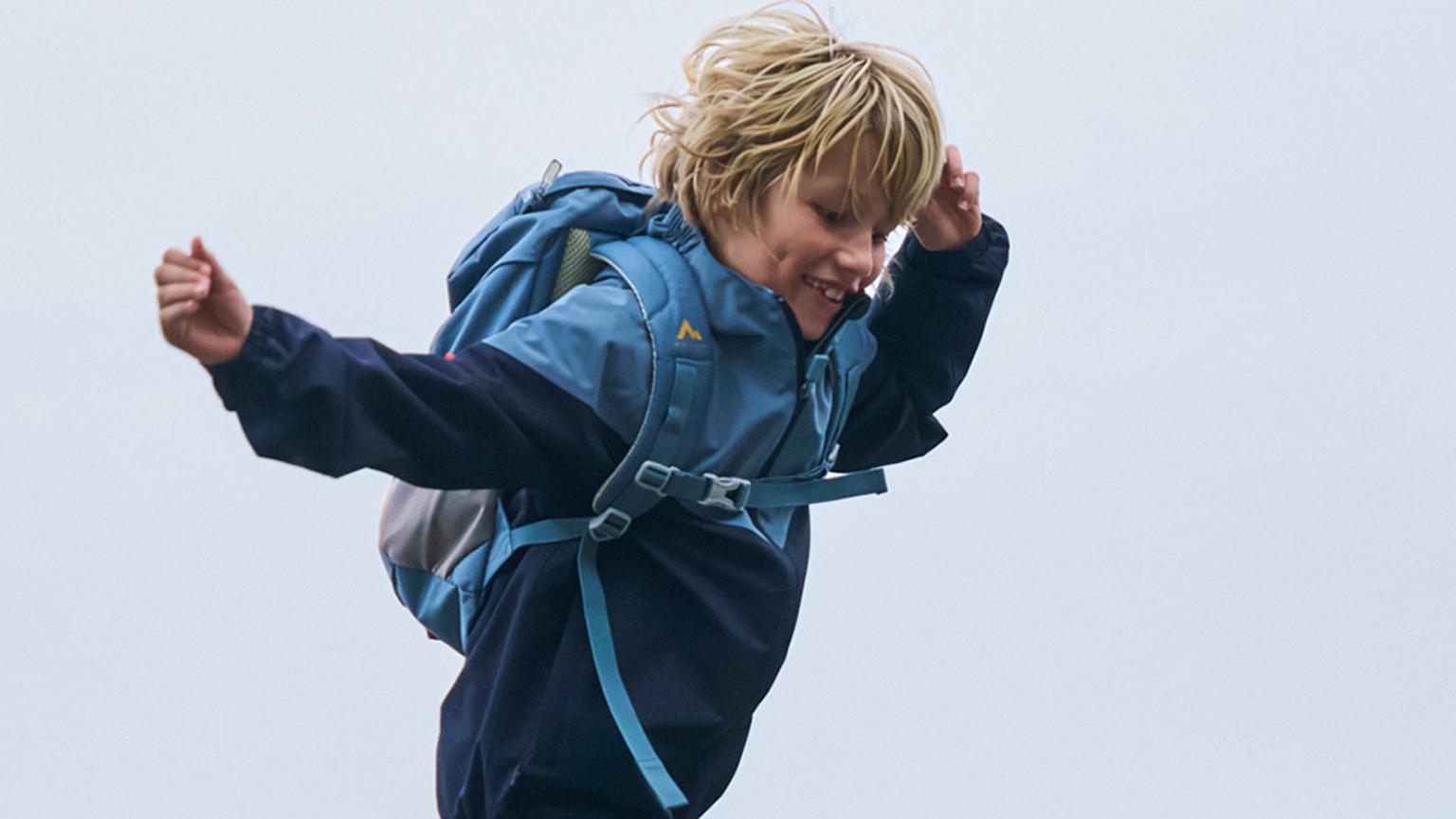 a young boy wearing a blue jacket and a backpack is jumping in the air .