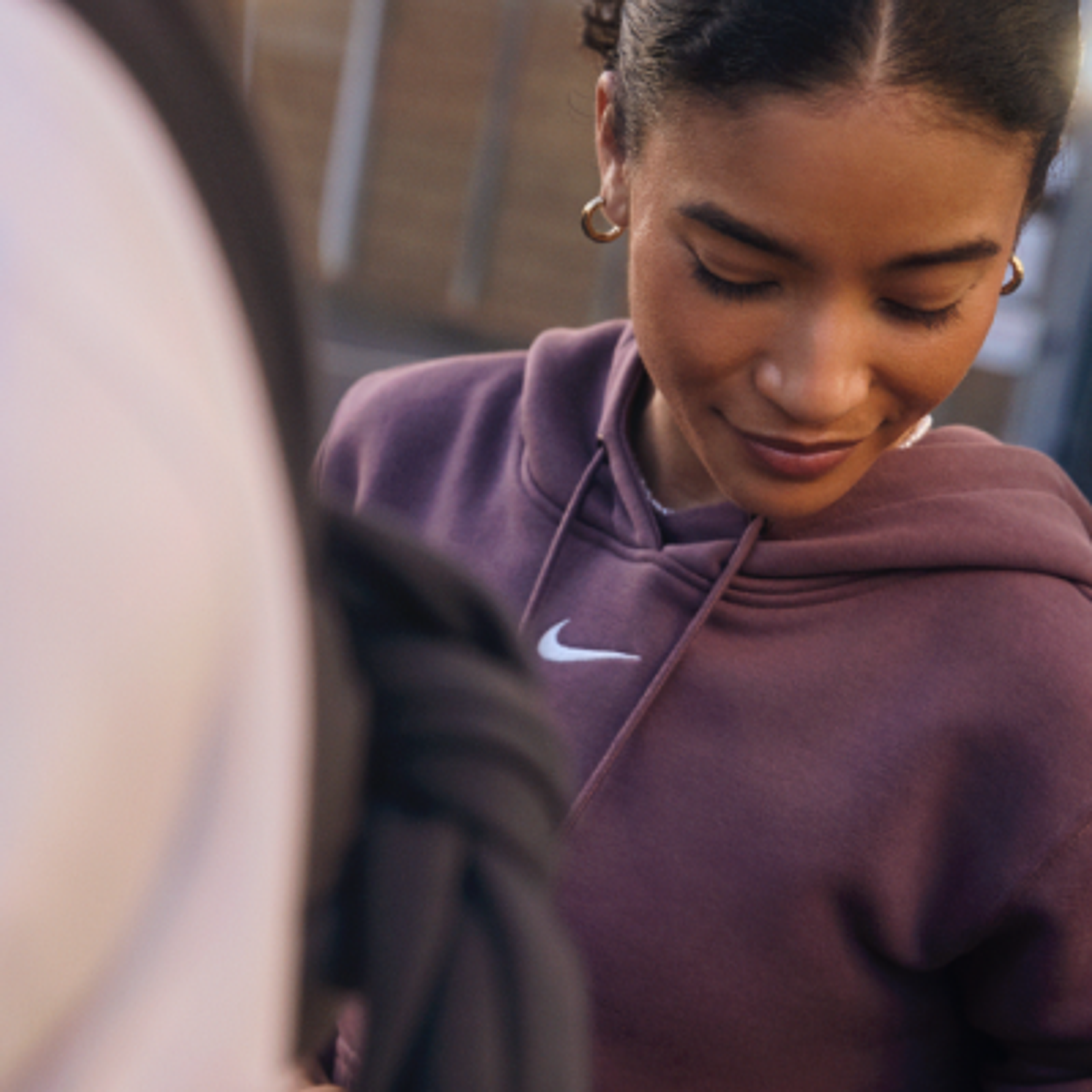 Woman in a plum Nike hoodie looking down with a slight smile.