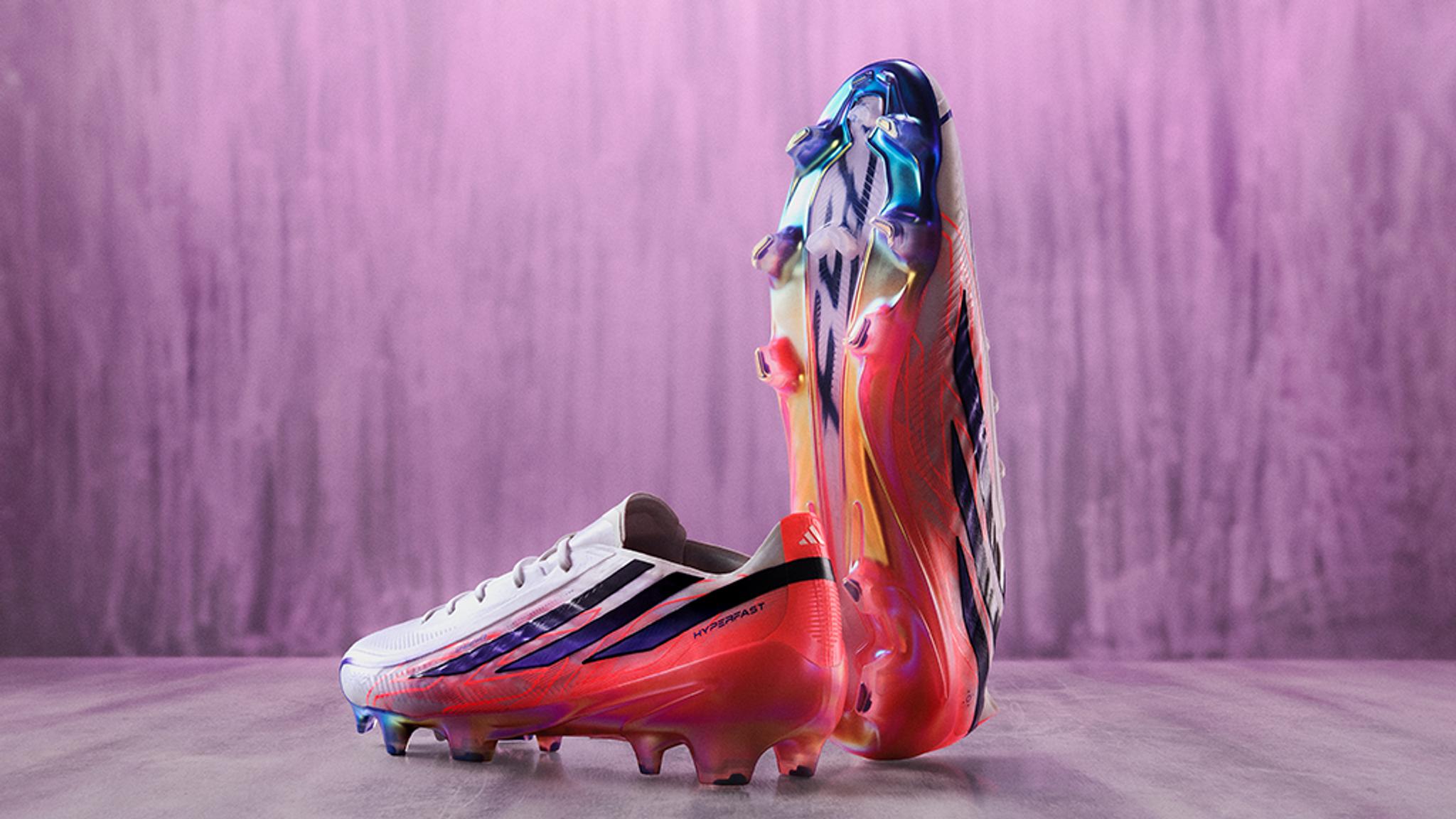 Two white, pink, and blue soccer cleats, one on its side and one upright, against a textured purple background.