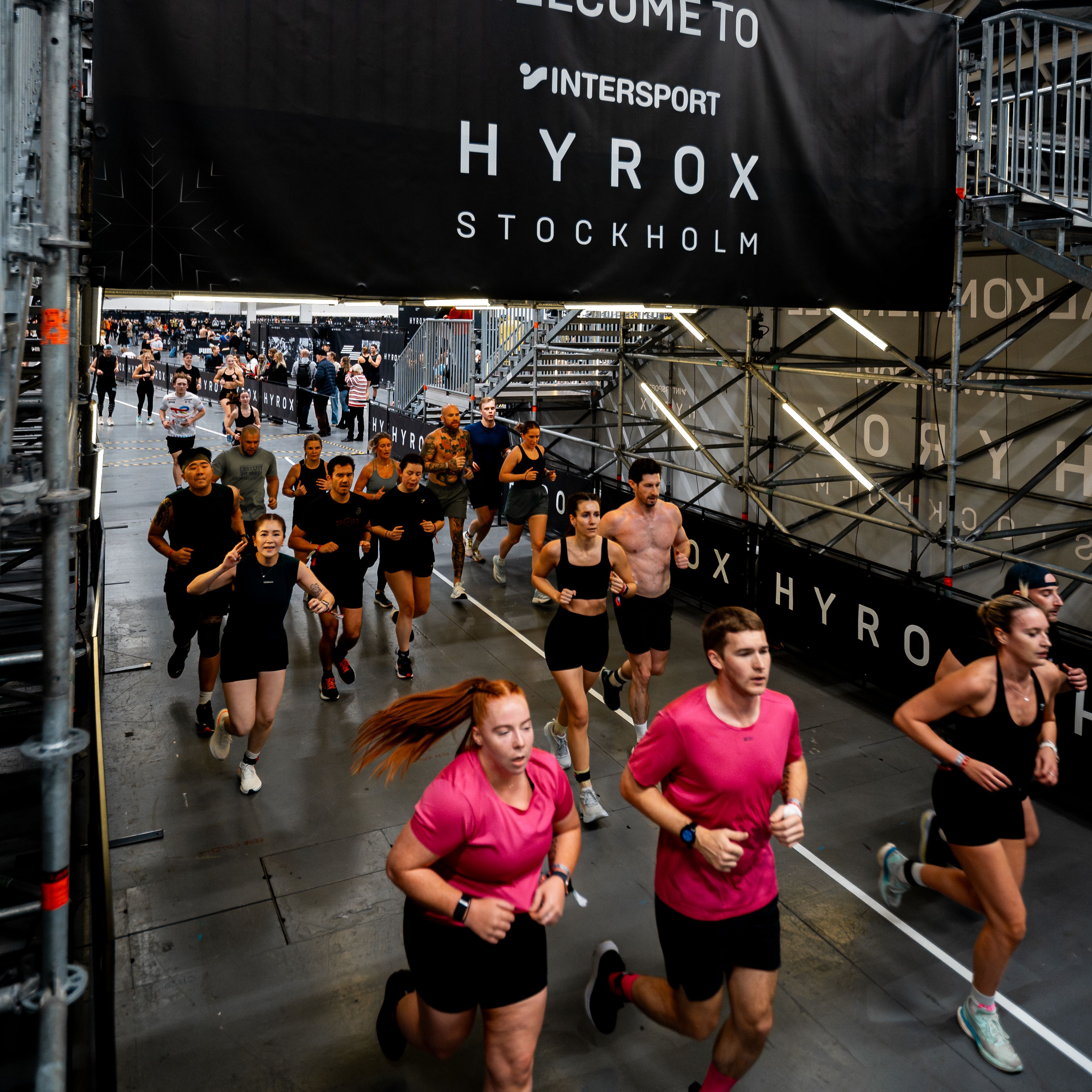 A group of people running indoors at a Hyrox Stockholm event, beneath a banner that reads "Welcome to Intersport Hyrox Stockholm".