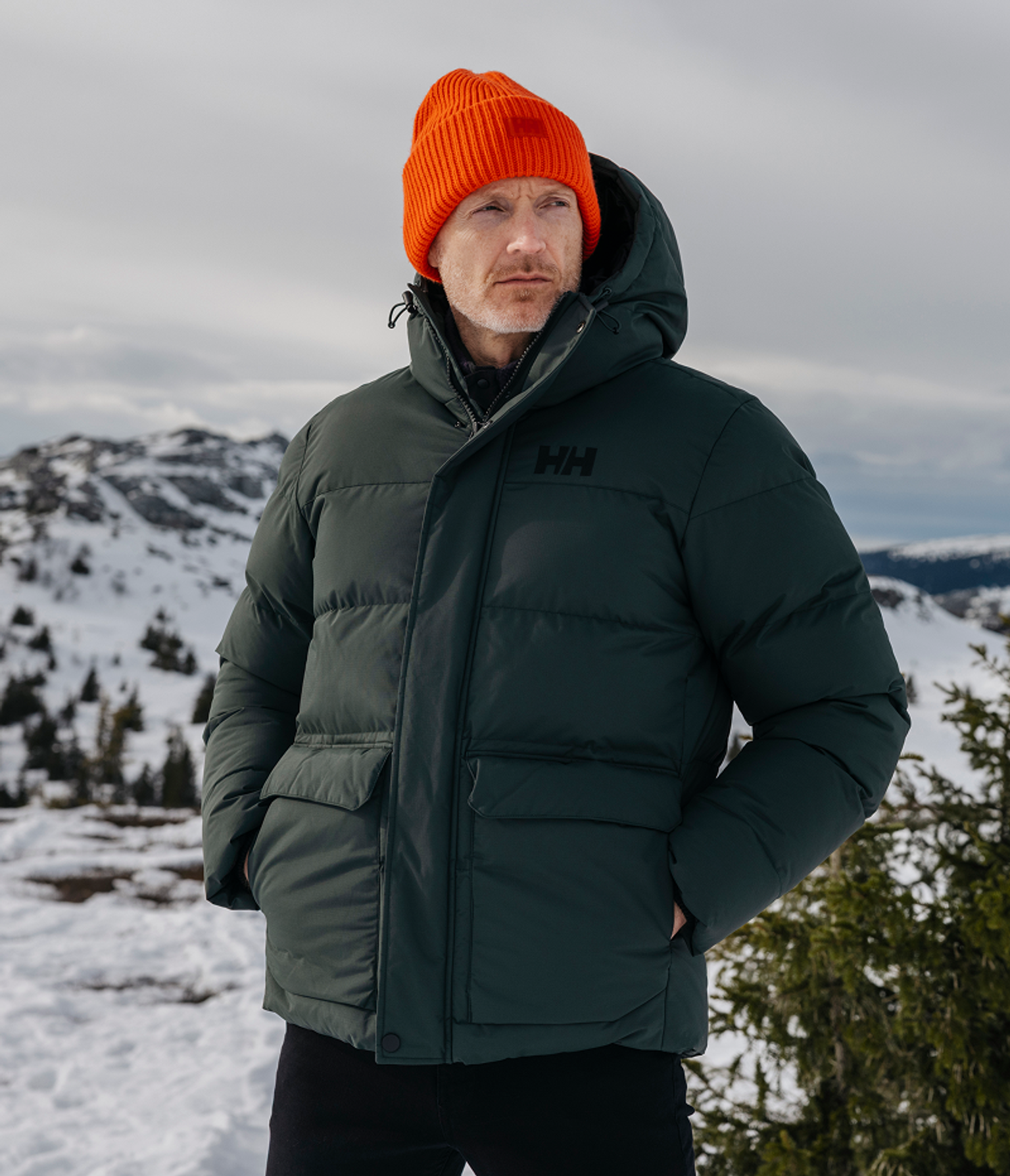 a man wearing an orange beanie and a green jacket that says hh