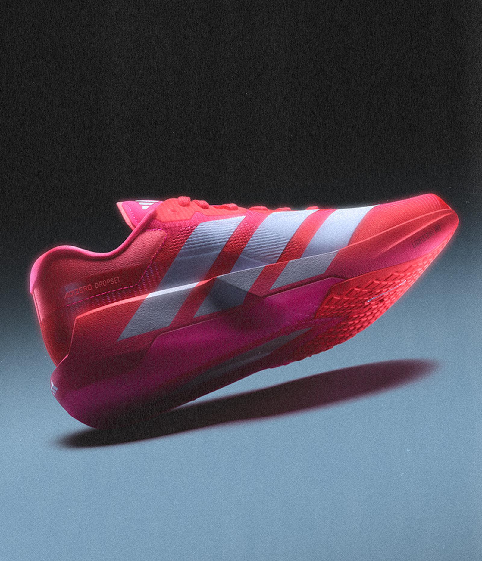 A vibrant pink and red Adidas ADIZERO DROPSET running shoe with white stripes, floating above a surface.