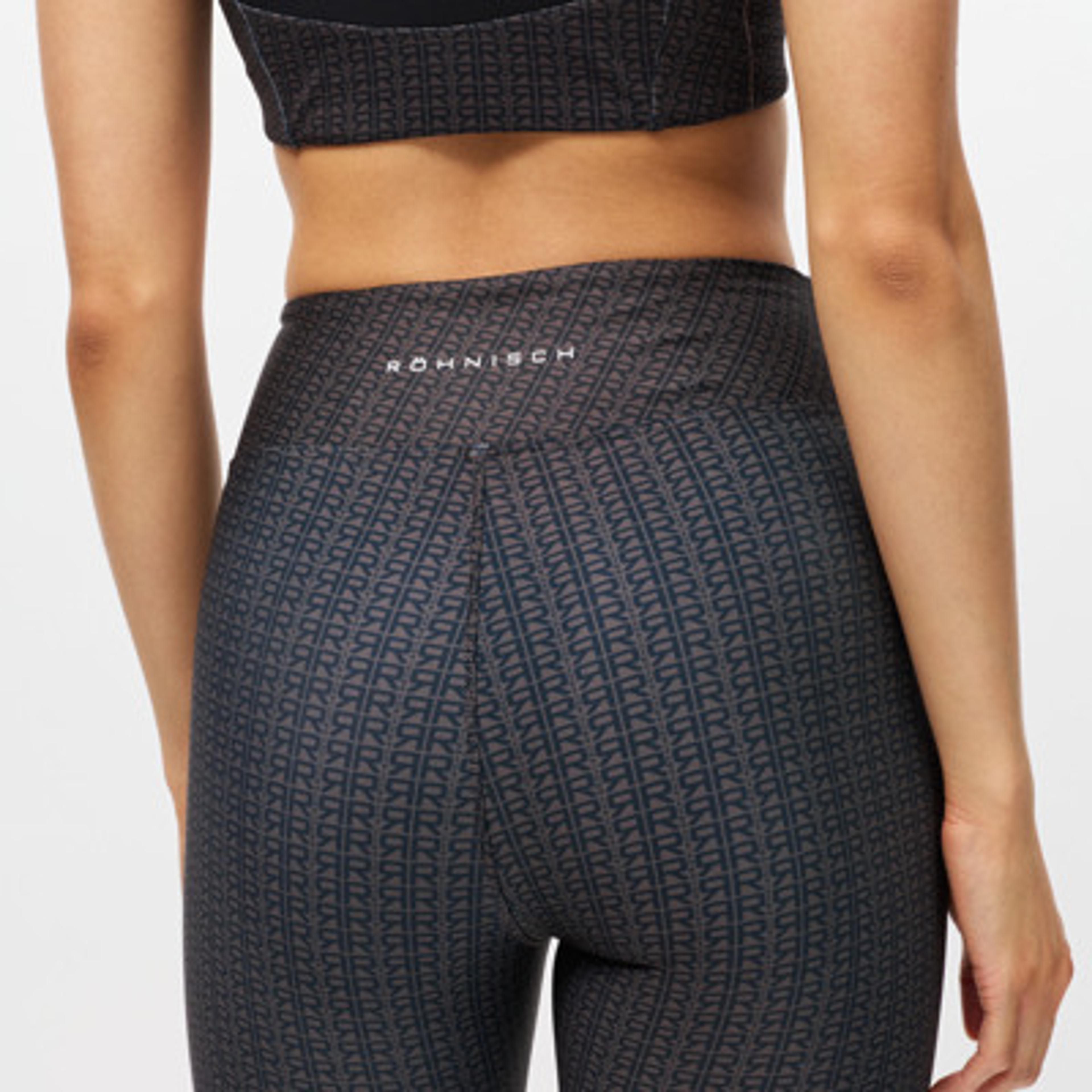 Back of a person wearing dark Röhnisch leggings with a repeating R pattern and a black sports bra.