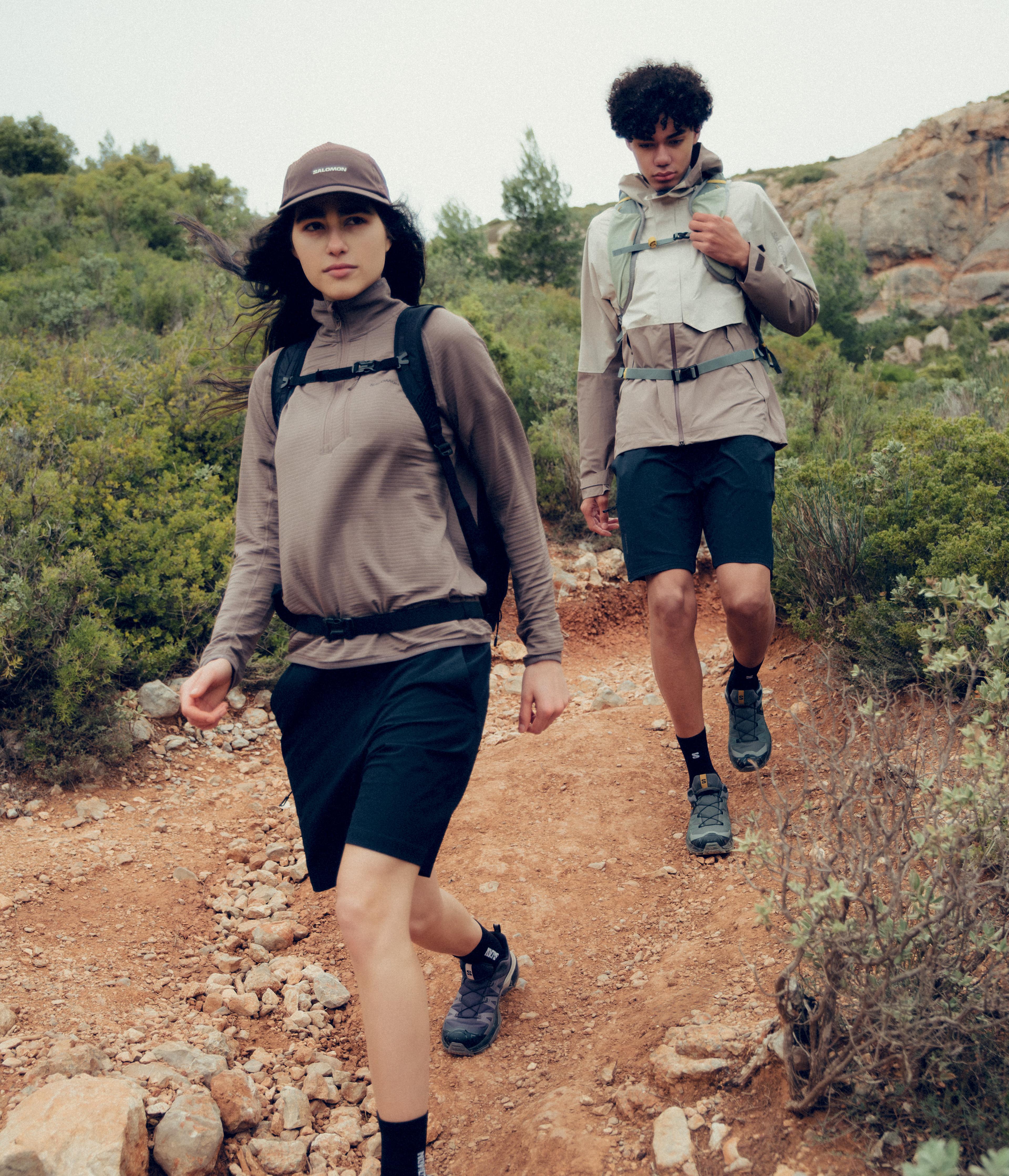 A woman and a man hiking on a rocky trail through brush.