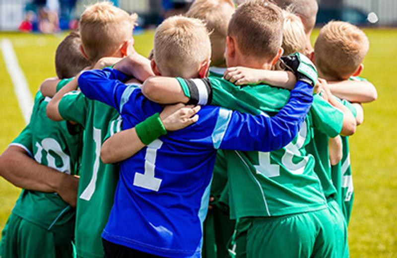 a group of young boys are hugging each other on a soccer field .