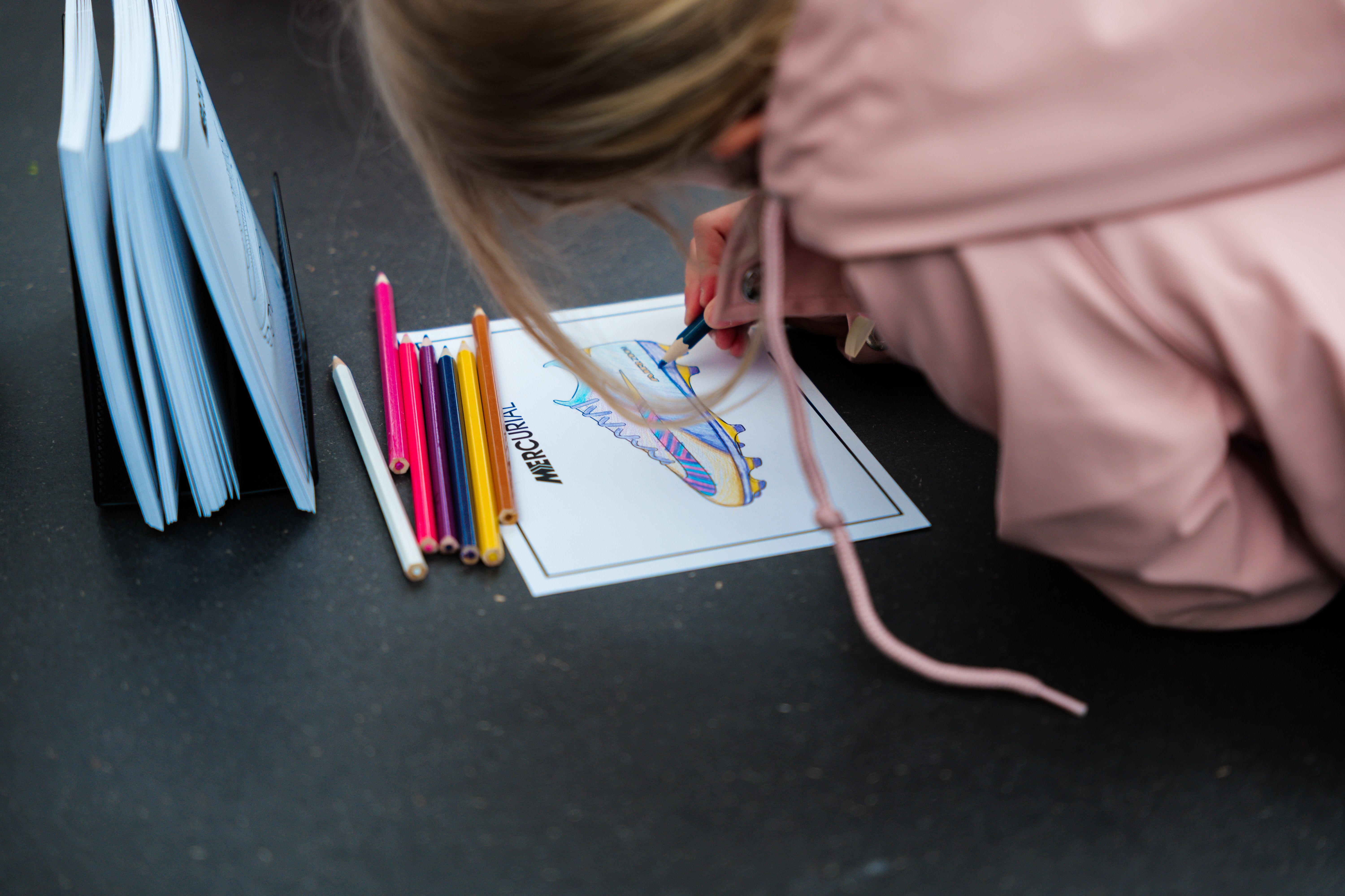 A person coloring a soccer cleat drawing with colored pencils.