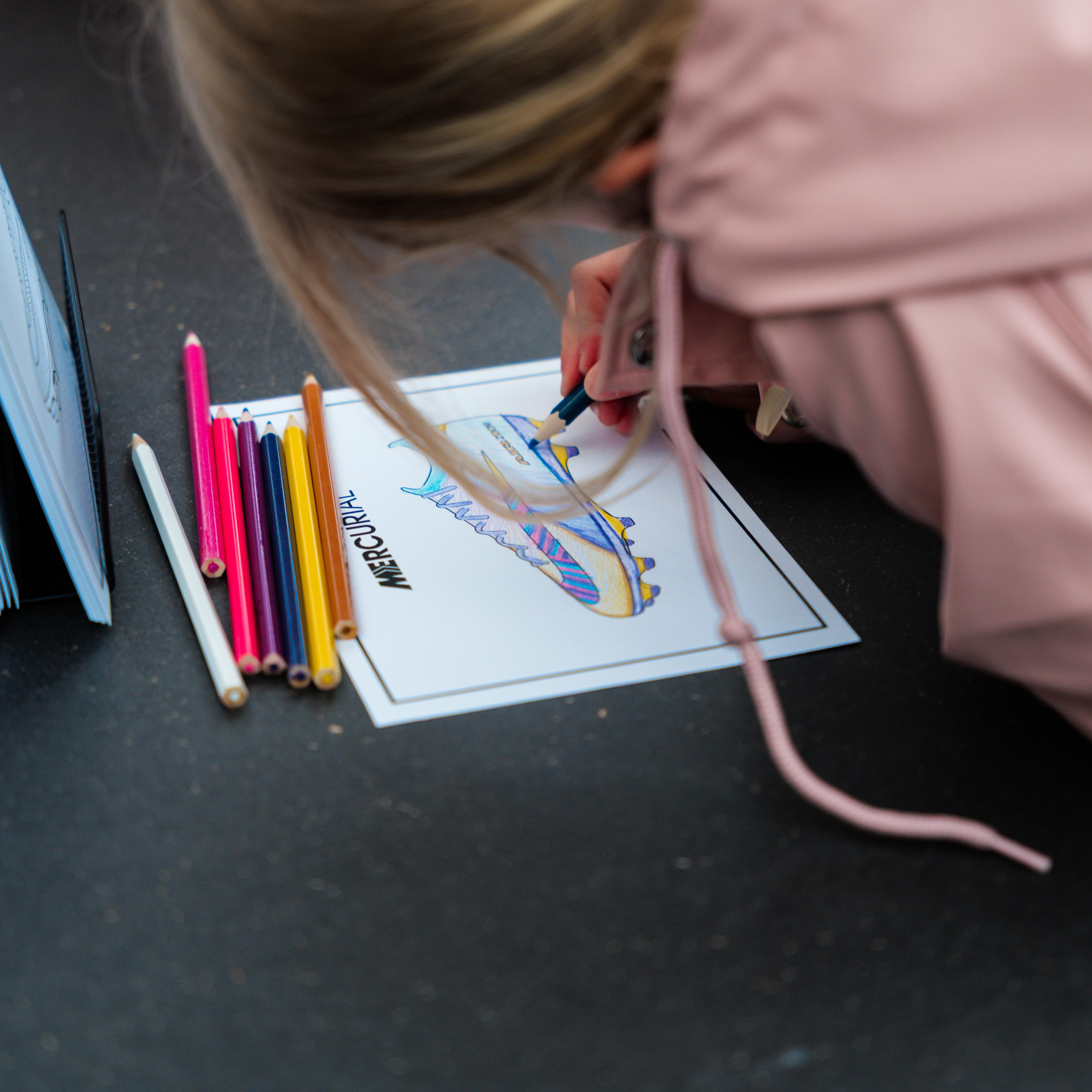 A person coloring a soccer cleat drawing with colored pencils.