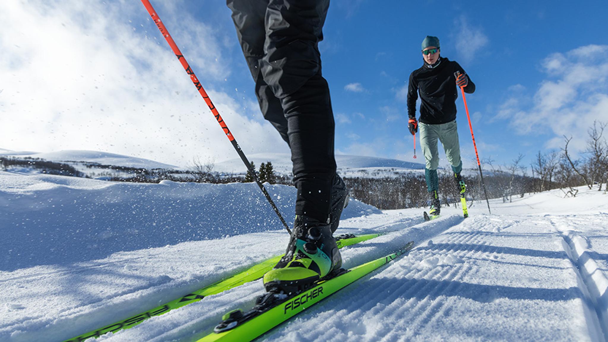 Two cross-country skiers on a groomed trail in a snowy, sunny landscape.