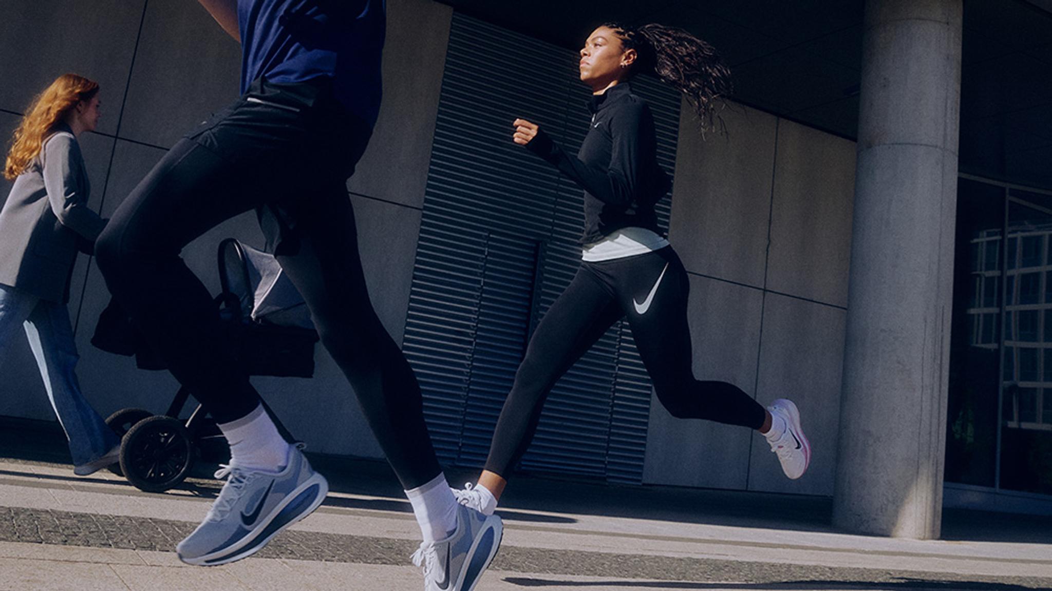 A man and woman running in Nike athletic wear on a city street.