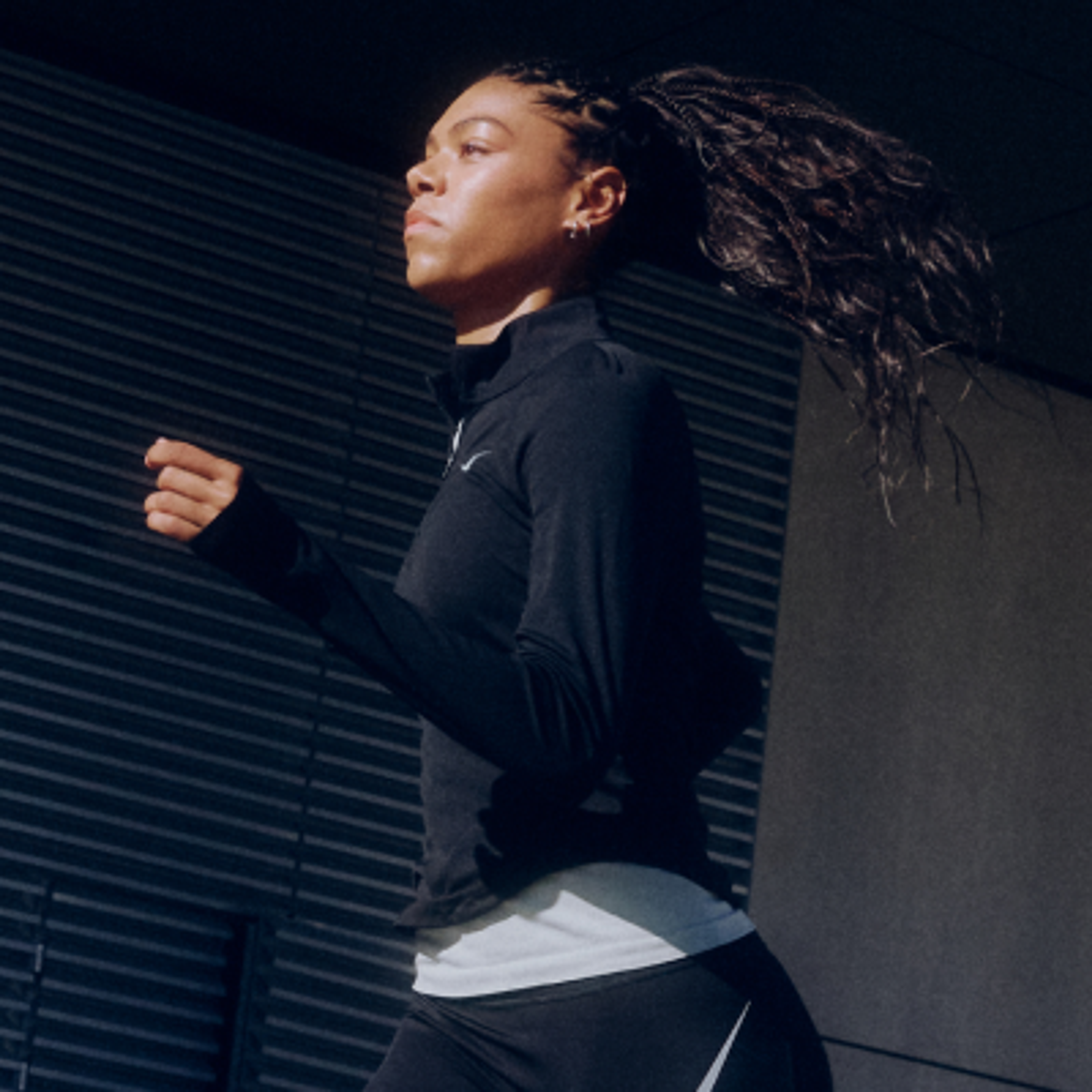 A woman with braided hair running in a black Nike long-sleeve top and leggings.