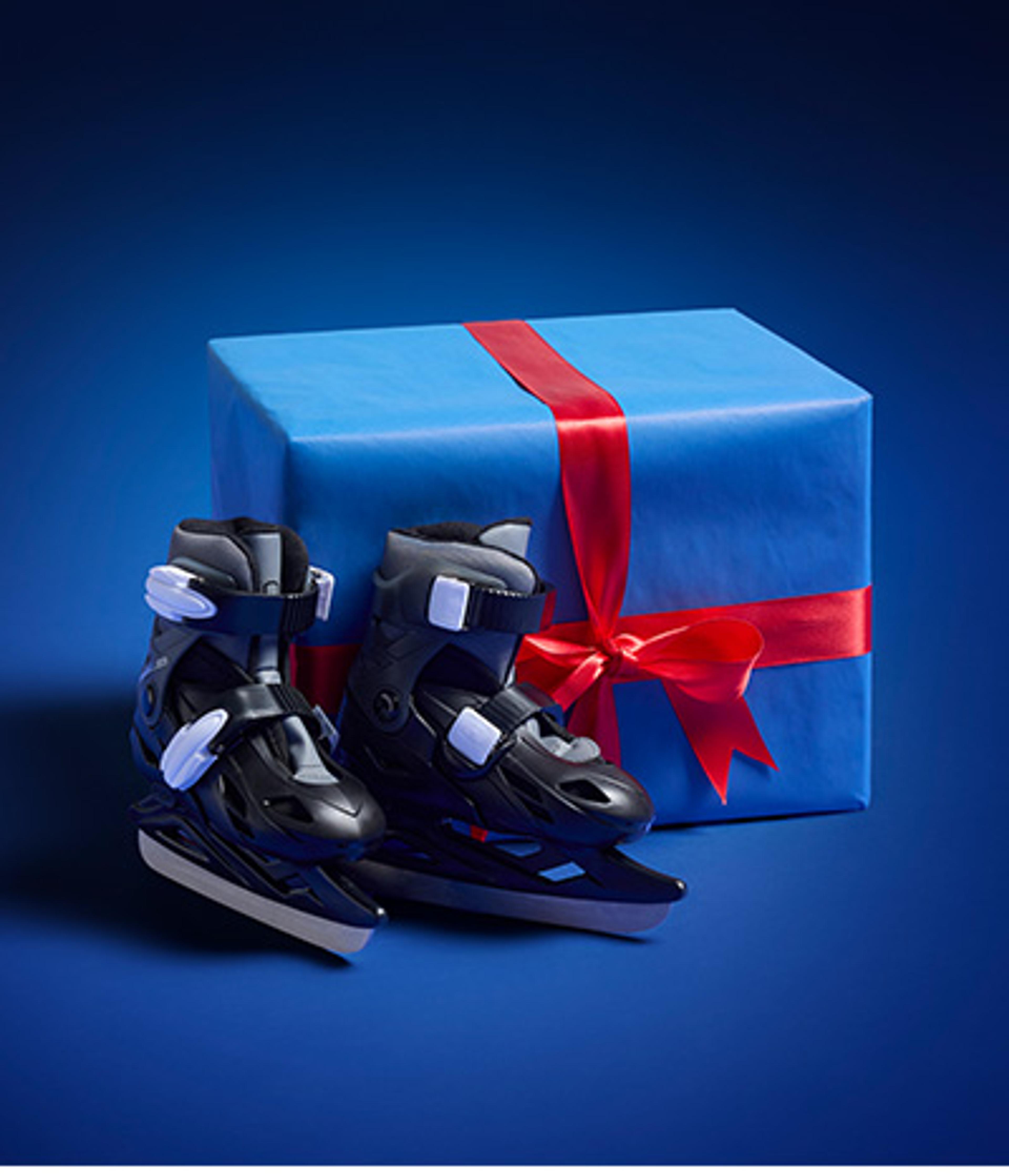 A pair of black ice skates rests beside a blue gift box tied with a red ribbon.