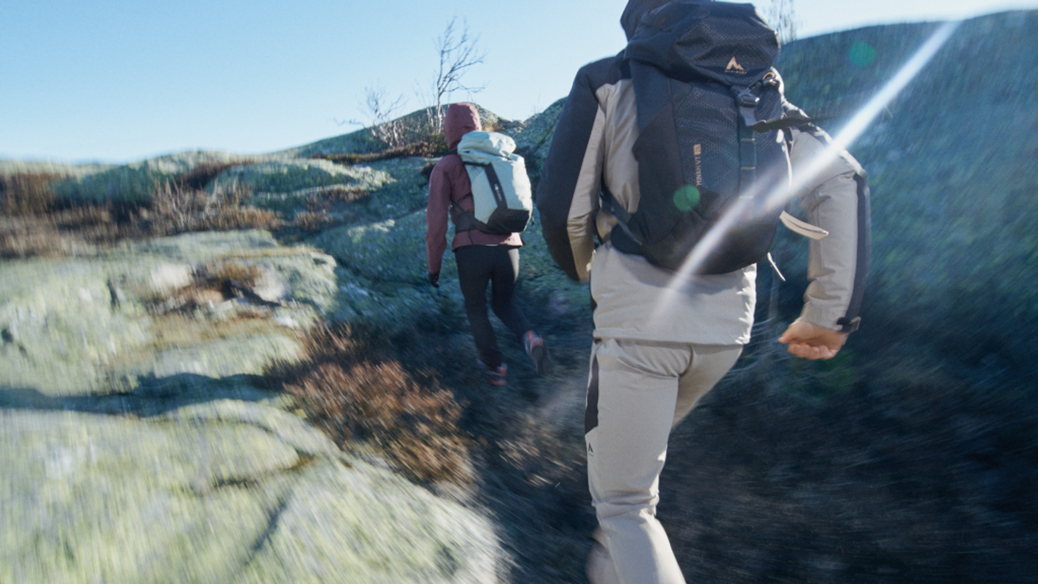 Two hikers with backpacks ascend a rocky hill at sunset.