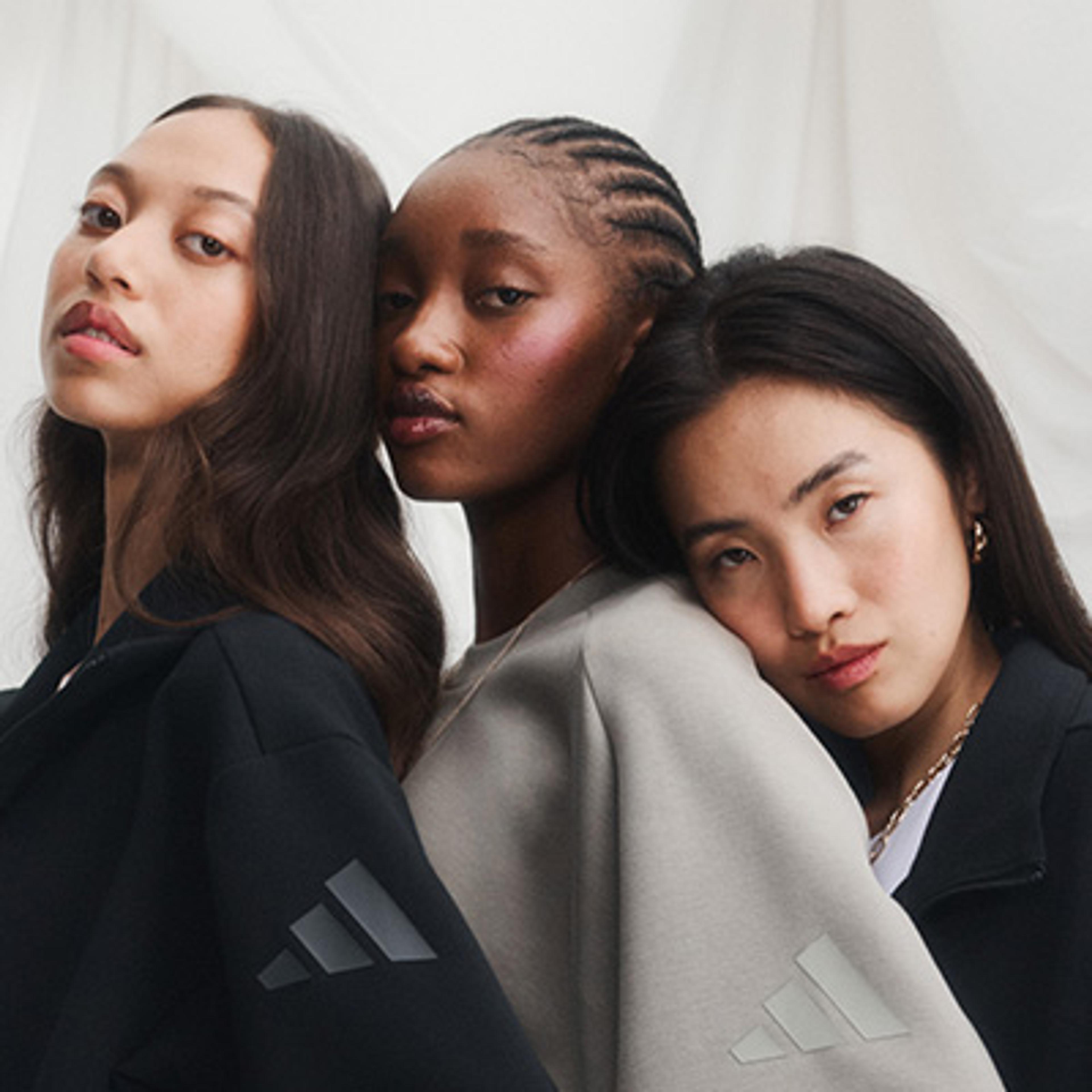 Three diverse women in Adidas sweatshirts look at the camera.