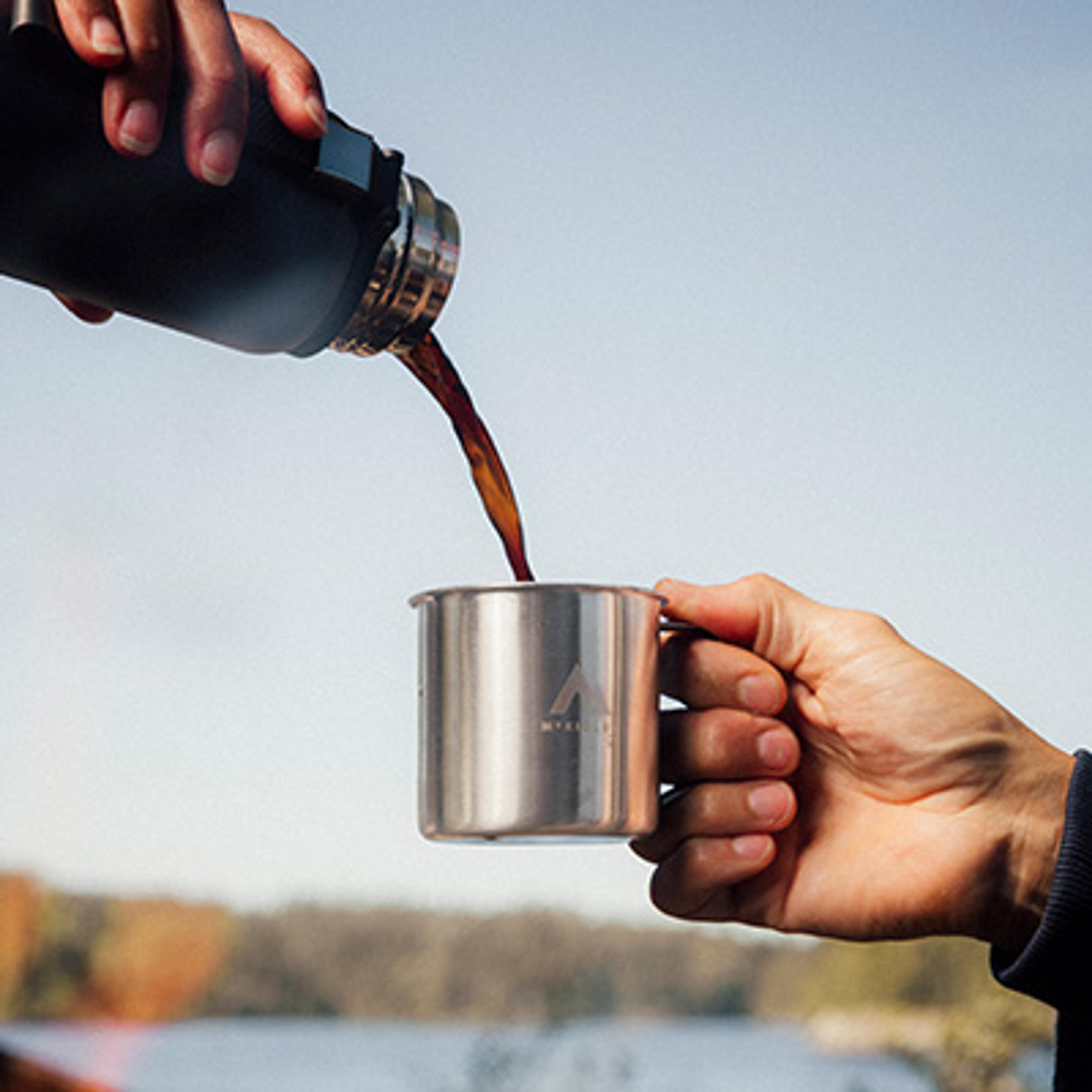 a person is pouring coffee into a stainless steel mug .