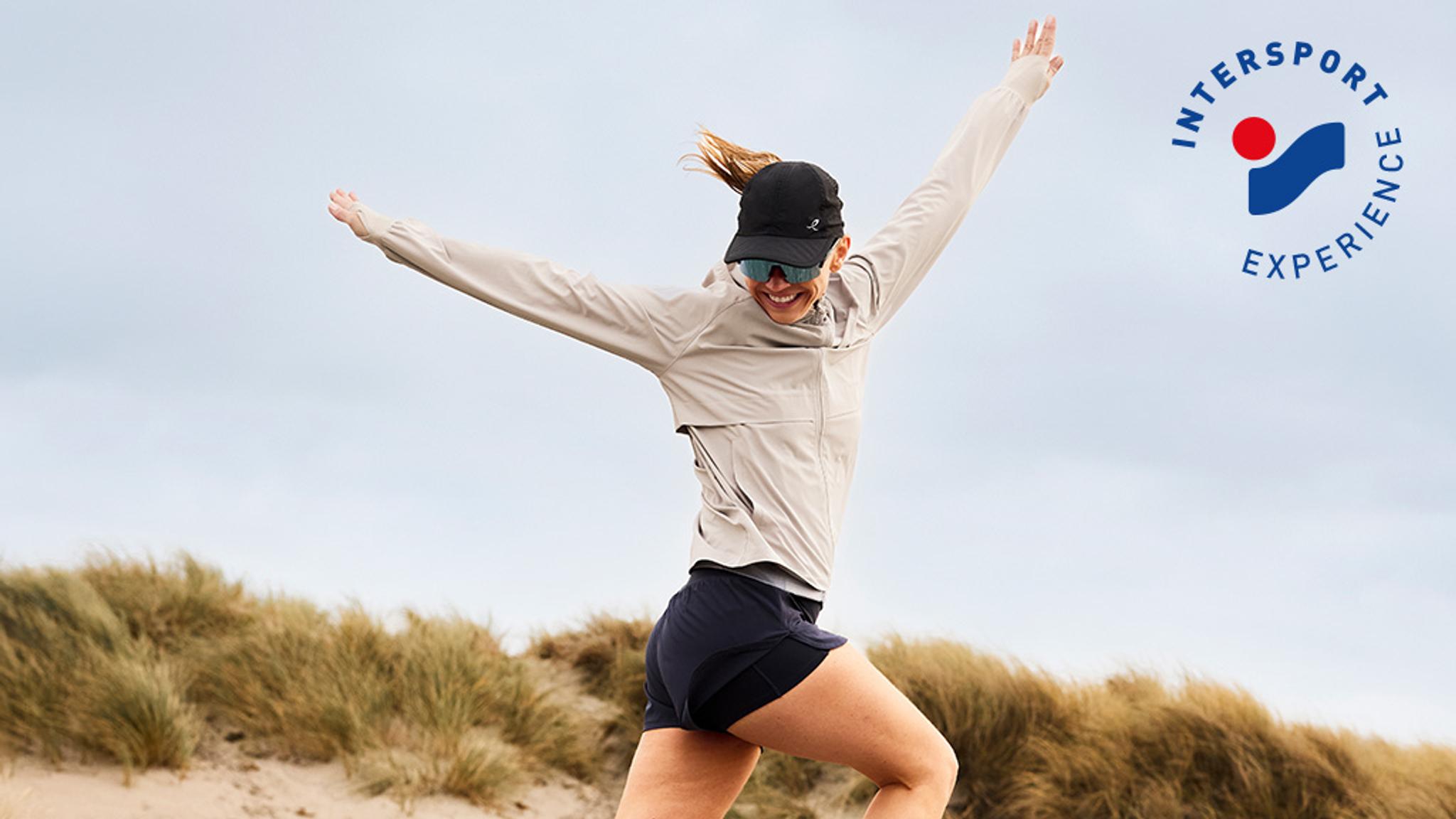 Woman leaps joyfully on dunes, Intersport Experience logo.